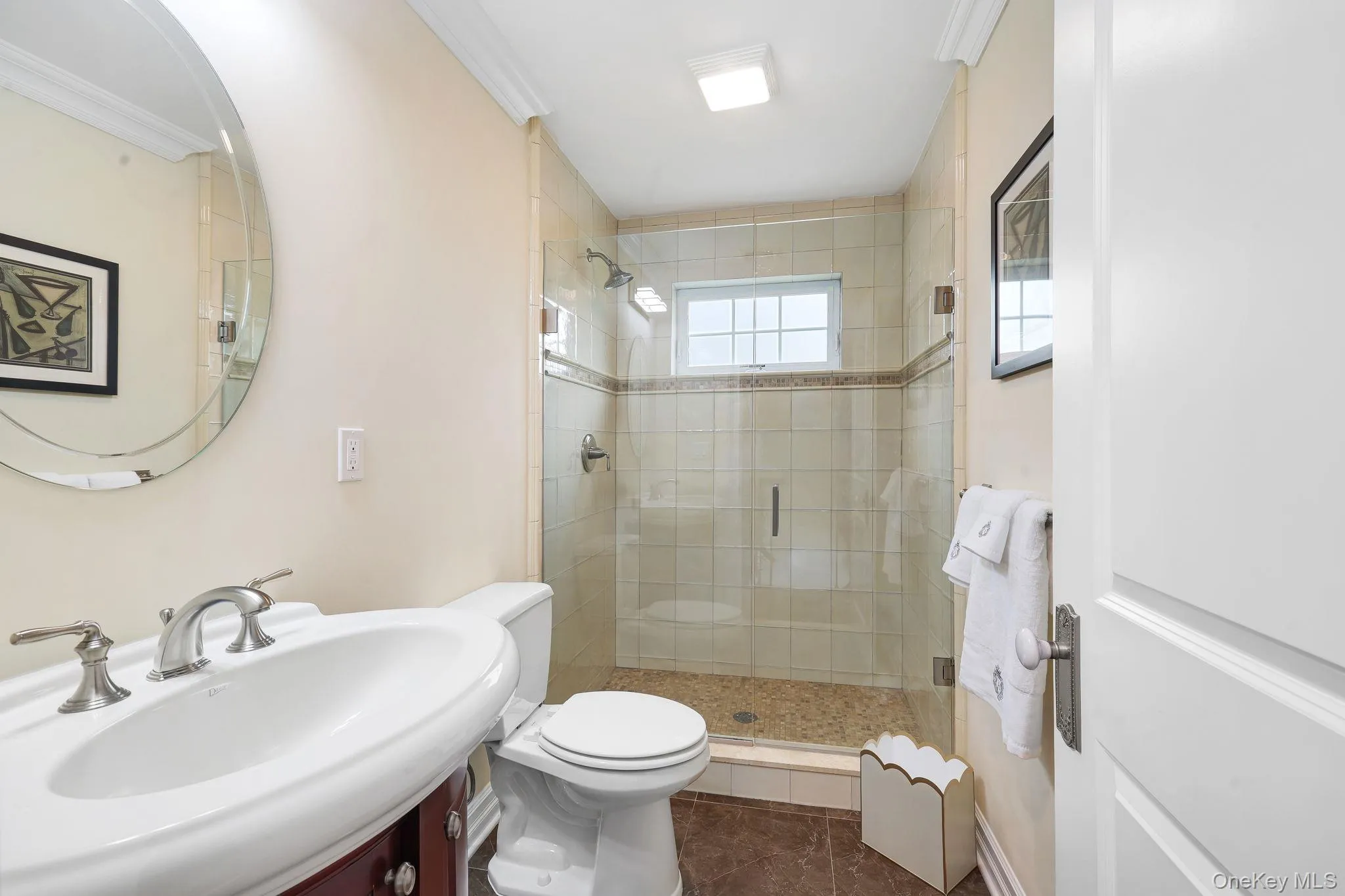 Upstairs elegant bathroom featuring a curved pedestal sink with chrome fixtures, ceramic tile shower enclosure with glass doors, white subway tile surround, and neutral tile flooring Upstairs elegant bathroom featuring a curved pedestal sink with chrome fixtures, ceramic tile shower enclosure with glass doors, white subway tile surround, and neutral tile flooring