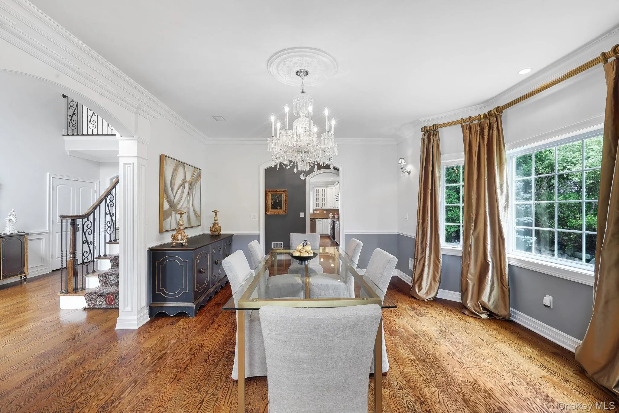 Hardwood flooring, chandelier with ceiling medallion, decorative wall sconces, columned archway, and wrought iron stair railing Hardwood flooring, chandelier with ceiling medallion, decorative wall sconces, columned archway, and wrought iron stair railing