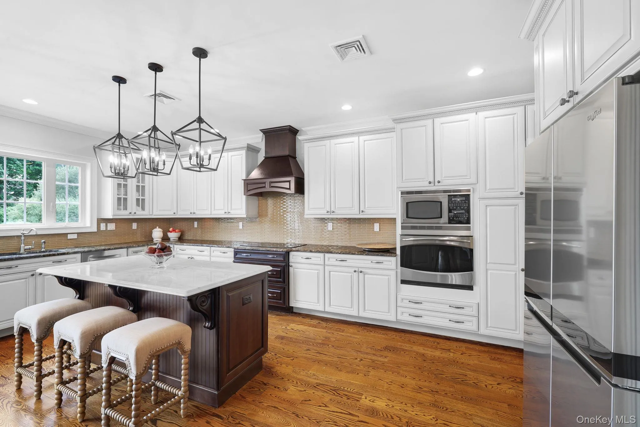 Kitchen featuring hardwood flooring, a central island with a light-toned countertop, white cabinetry, a built-in microwave and oven, and stainless steel refrigerator Kitchen featuring hardwood flooring, a central island with a light-toned countertop, white cabinetry, a built-in microwave and oven, and stainless steel refrigerator