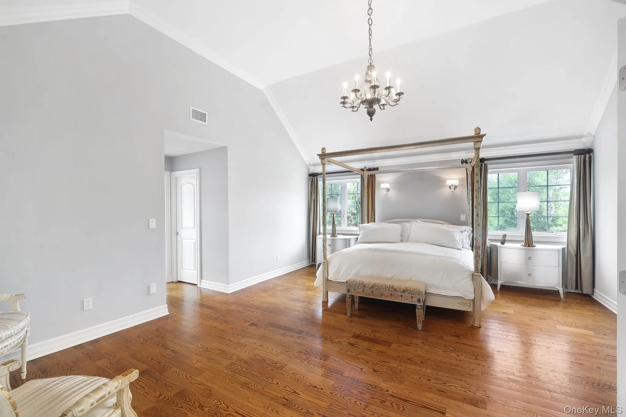 Oversized with vaulted ceiling with crown molding, wood-finish flooring, multiple windows, and a chandelier Oversized with vaulted ceiling with crown molding, wood-finish flooring, multiple windows, and a chandelier
