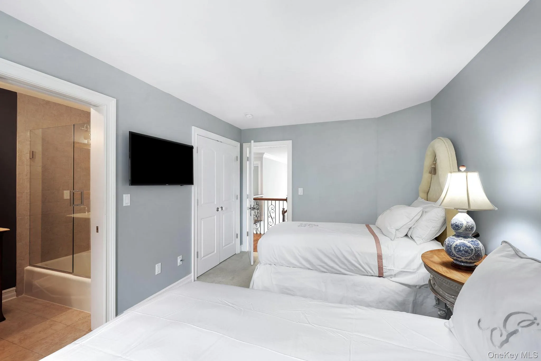 Light-toned wall paint, light wood-finish flooring, white paneled doors, and an en-suite bathroom with a glass-enclosed shower over tub Light-toned wall paint, light wood-finish flooring, white paneled doors, and an en-suite bathroom with a glass-enclosed shower over tub