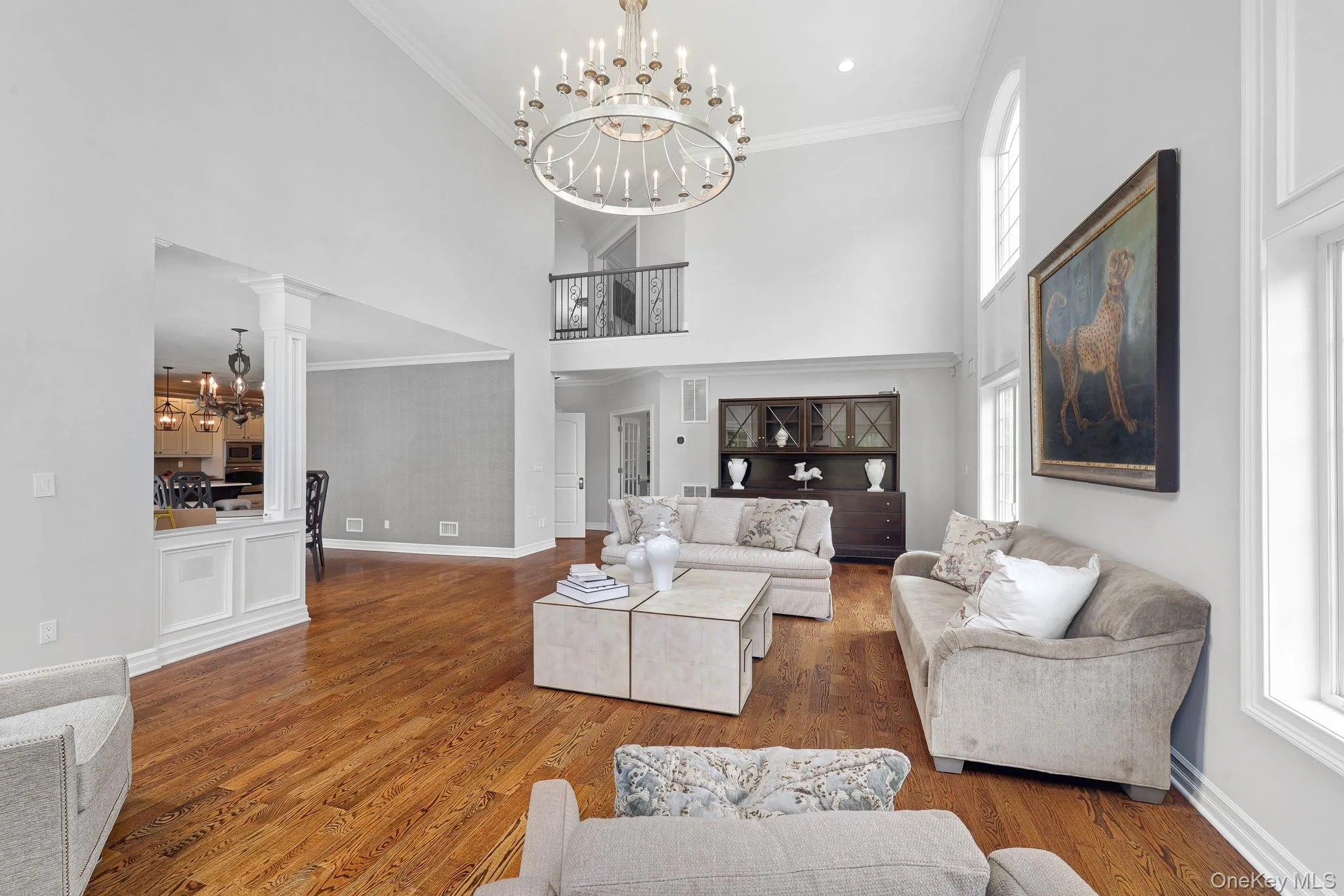 Two-story living area featuring hardwood flooring, a multi-tiered chandelier, tall arched windows, and a second-story balcony Two-story living area featuring hardwood flooring, a multi-tiered chandelier, tall arched windows, and a second-story balcony