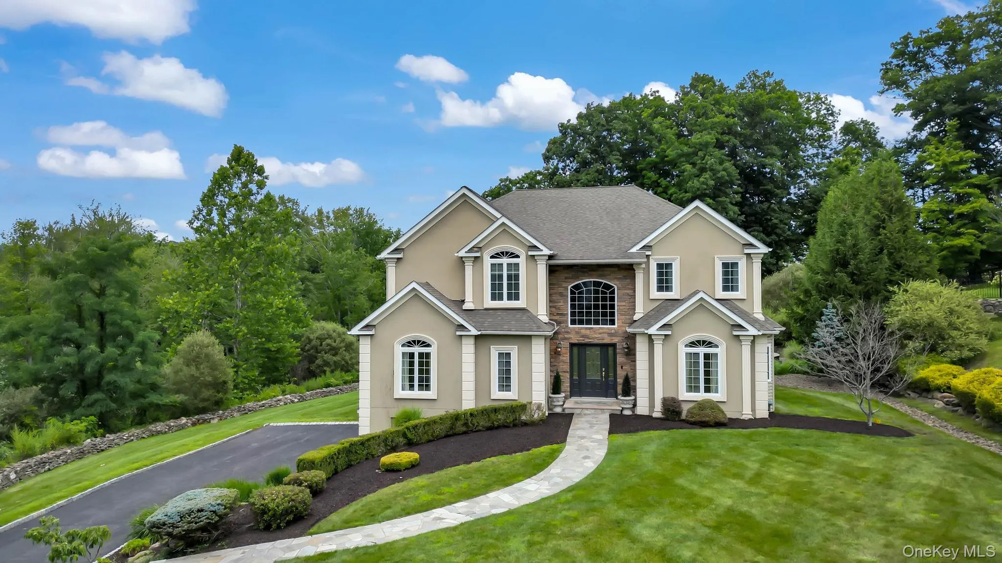 Stately two-story Colonial with cream exterior and dark roof, featuring a symmetrical facade with multiple arched and rectangular windows, a centered brick entry vestibule with arched doorway, and a curved driveway Stately two-story Colonial with cream exterior and dark roof, featuring a symmetrical facade with multiple arched and rectangular windows, a centered brick entry vestibule with arched doorway, and a curved driveway