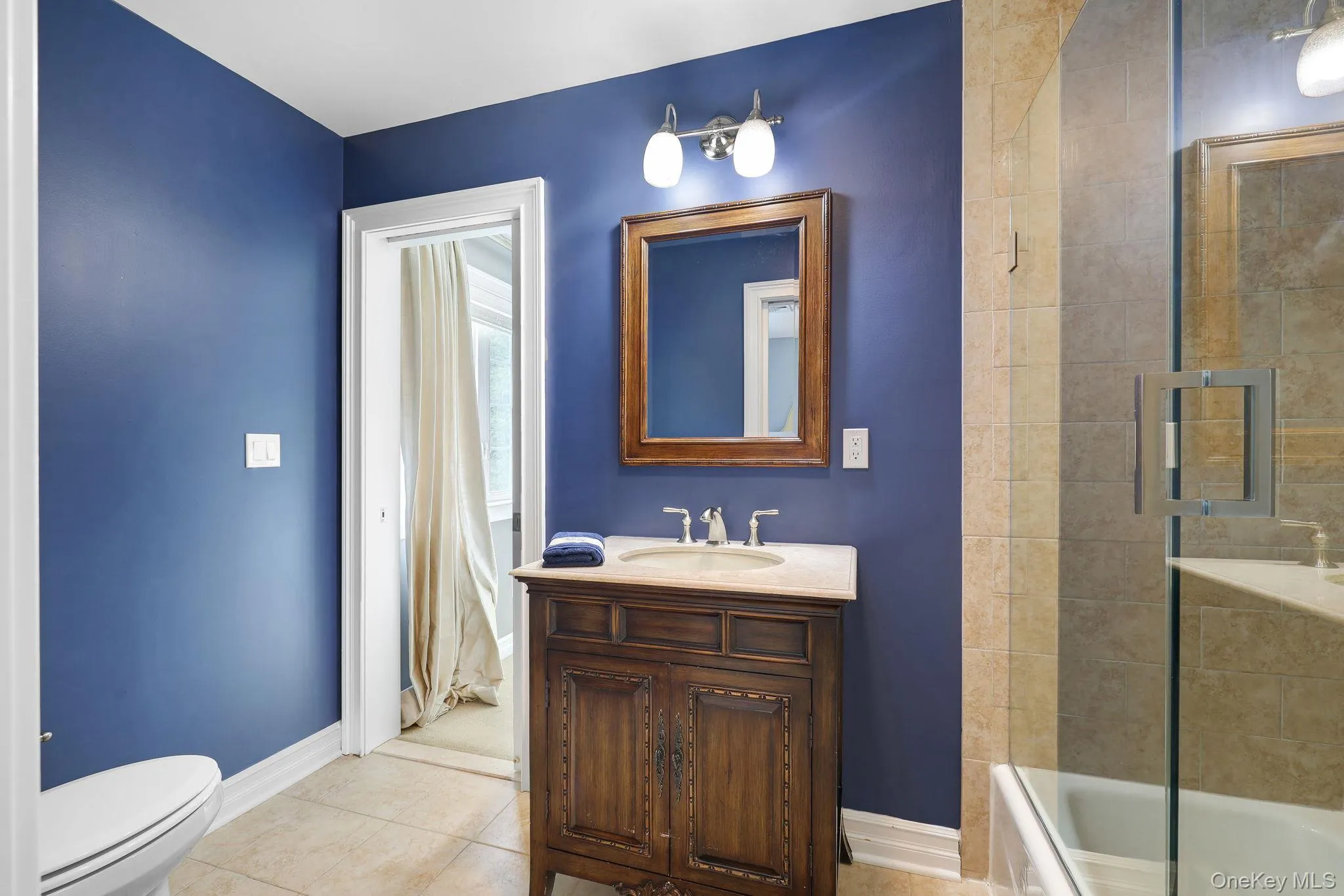 Jack and jill, bathroom hardwood vanity with a light-colored countertop, framed mirror, and a two-light fixture Jack and jill, bathroom hardwood vanity with a light-colored countertop, framed mirror, and a two-light fixture