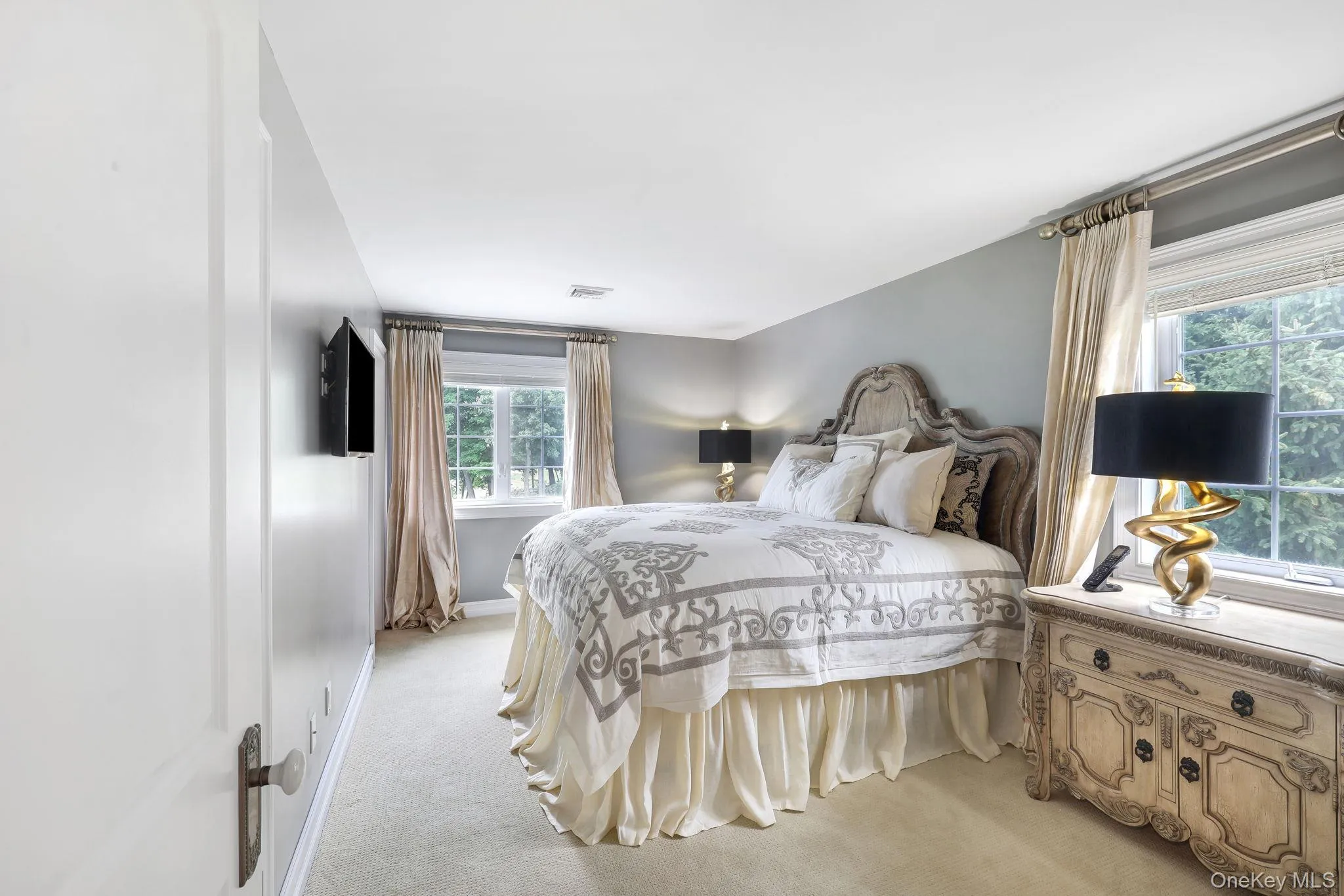 Wall-mounted television with an ornate headboard, light gray walls, and large windows Wall-mounted television with an ornate headboard, light gray walls, and large windows