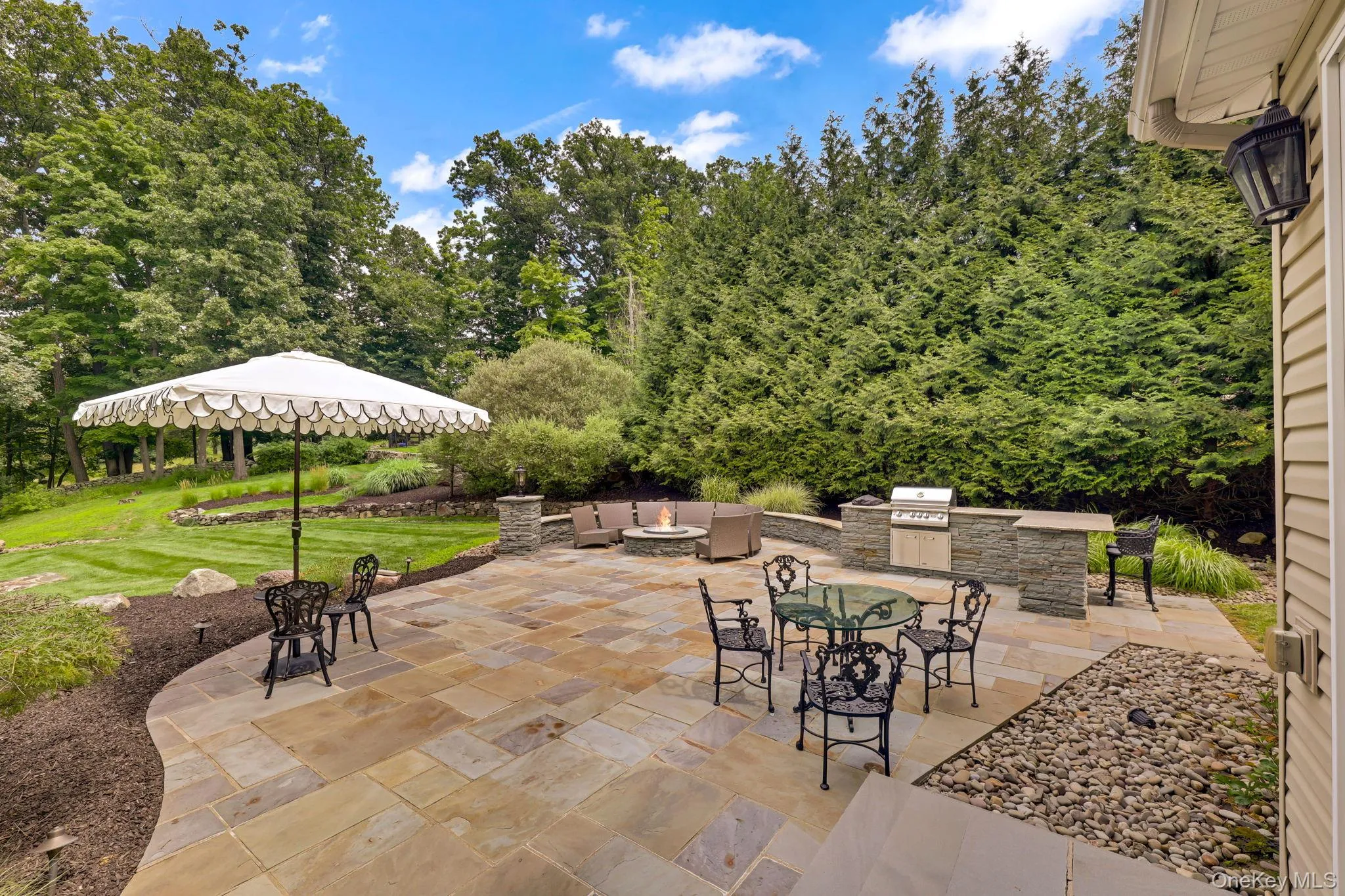 Expansive stone patio with a built-in outdoor kitchen, integrated fire pit, and stone retaining wall Expansive stone patio with a built-in outdoor kitchen, integrated fire pit, and stone retaining wall