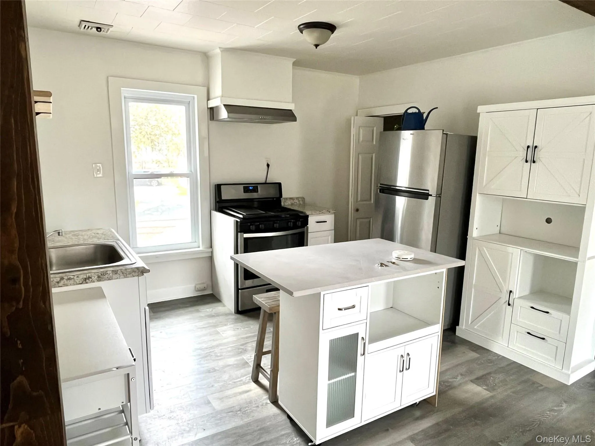 Kitchen featuring stainless steel appliances, a center island with storage, white cabinetry, and wood-finish flooring Kitchen featuring stainless steel appliances, a center island with storage, white cabinetry, and wood-finish flooring