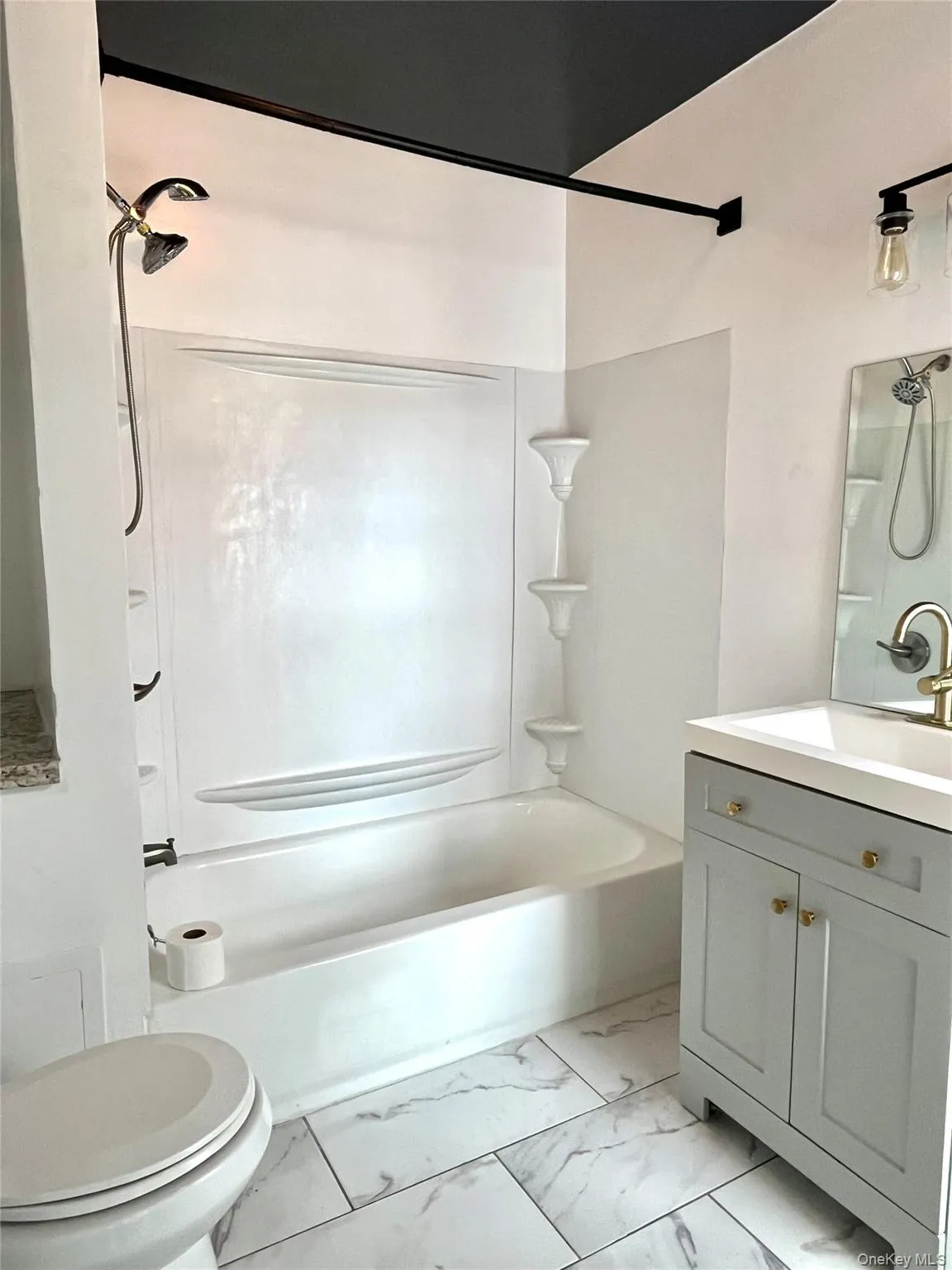 Bathroom featuring a white tub and shower combination, a light gray vanity with a white basin, a mounted mirror, and large format marble-look floor tiles Bathroom featuring a white tub and shower combination, a light gray vanity with a white basin, a mounted mirror, and large format marble-look floor tiles