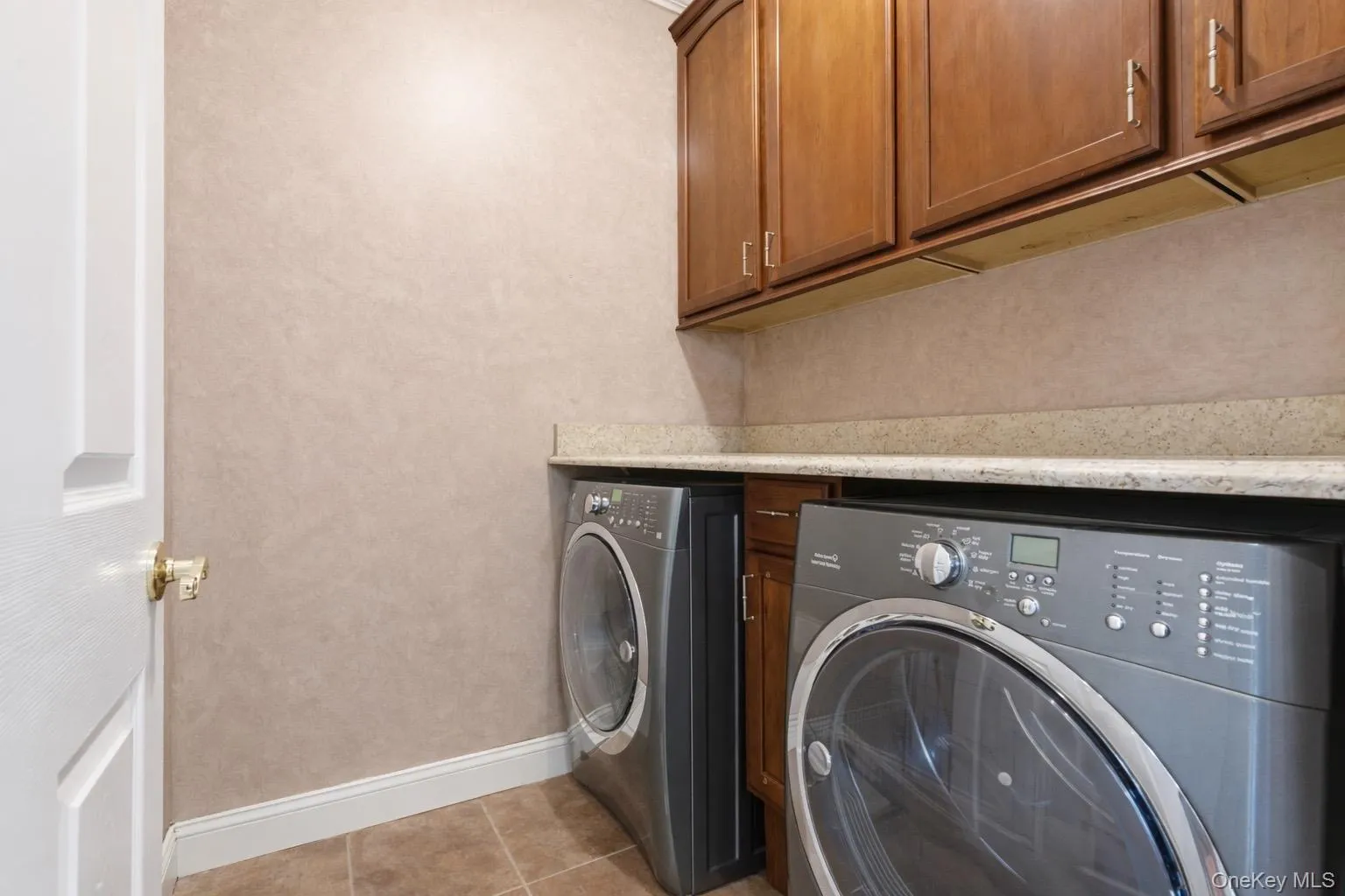 Laundry area featuring wood cabinetry, a light-colored countertop, and tiled flooring Laundry area featuring wood cabinetry, a light-colored countertop, and tiled flooring
