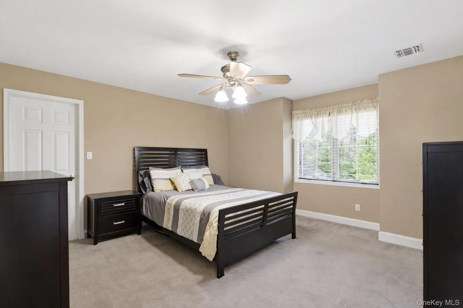 This room features neutral-toned walls, light-colored carpeting, a window with natural light, and a ceiling fan with integrated lighting This room features neutral-toned walls, light-colored carpeting, a window with natural light, and a ceiling fan with integrated lighting