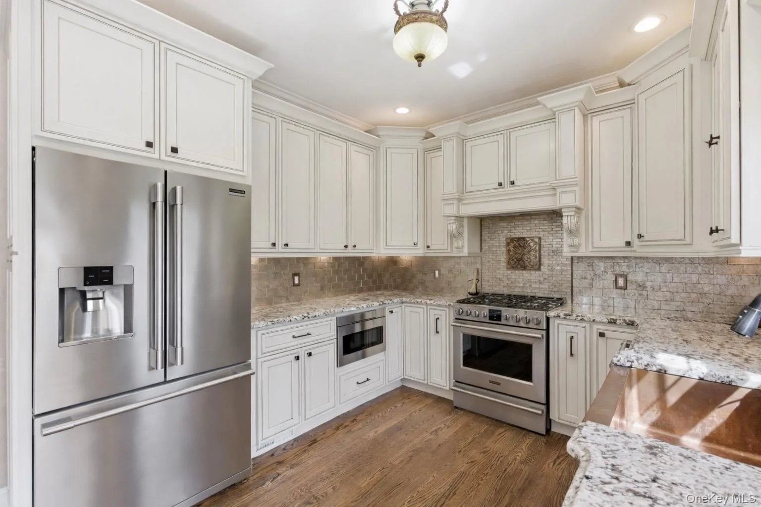 The kitchen features hardwood flooring, white cabinetry, granite countertops, and stainless steel appliances including a refrigerator, oven, and microwave The kitchen features hardwood flooring, white cabinetry, granite countertops, and stainless steel appliances including a refrigerator, oven, and microwave
