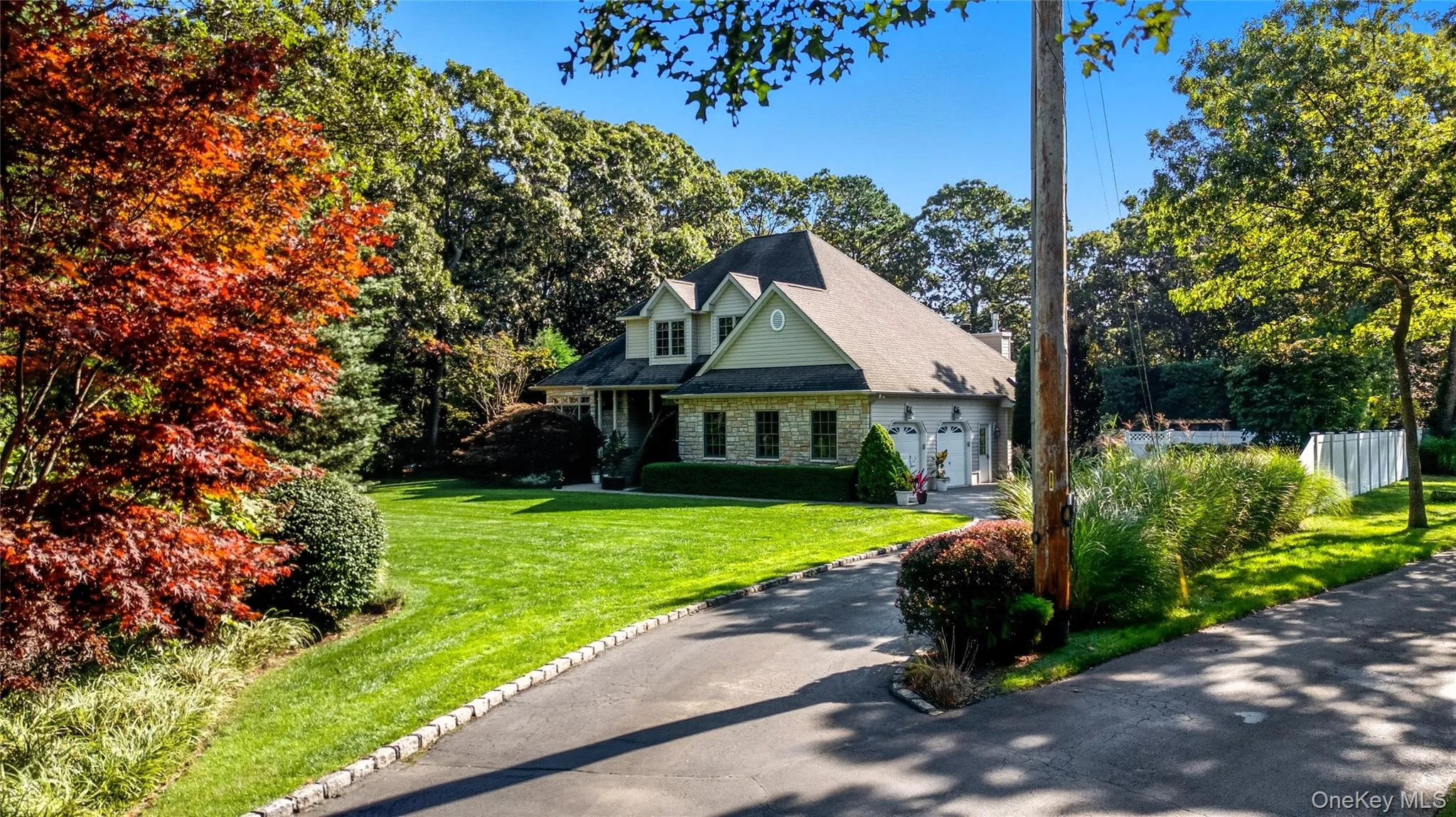 View of front of property with a front lawn, stone siding, and view of wooded area View of front of property with a front lawn, stone siding, and view of wooded area
