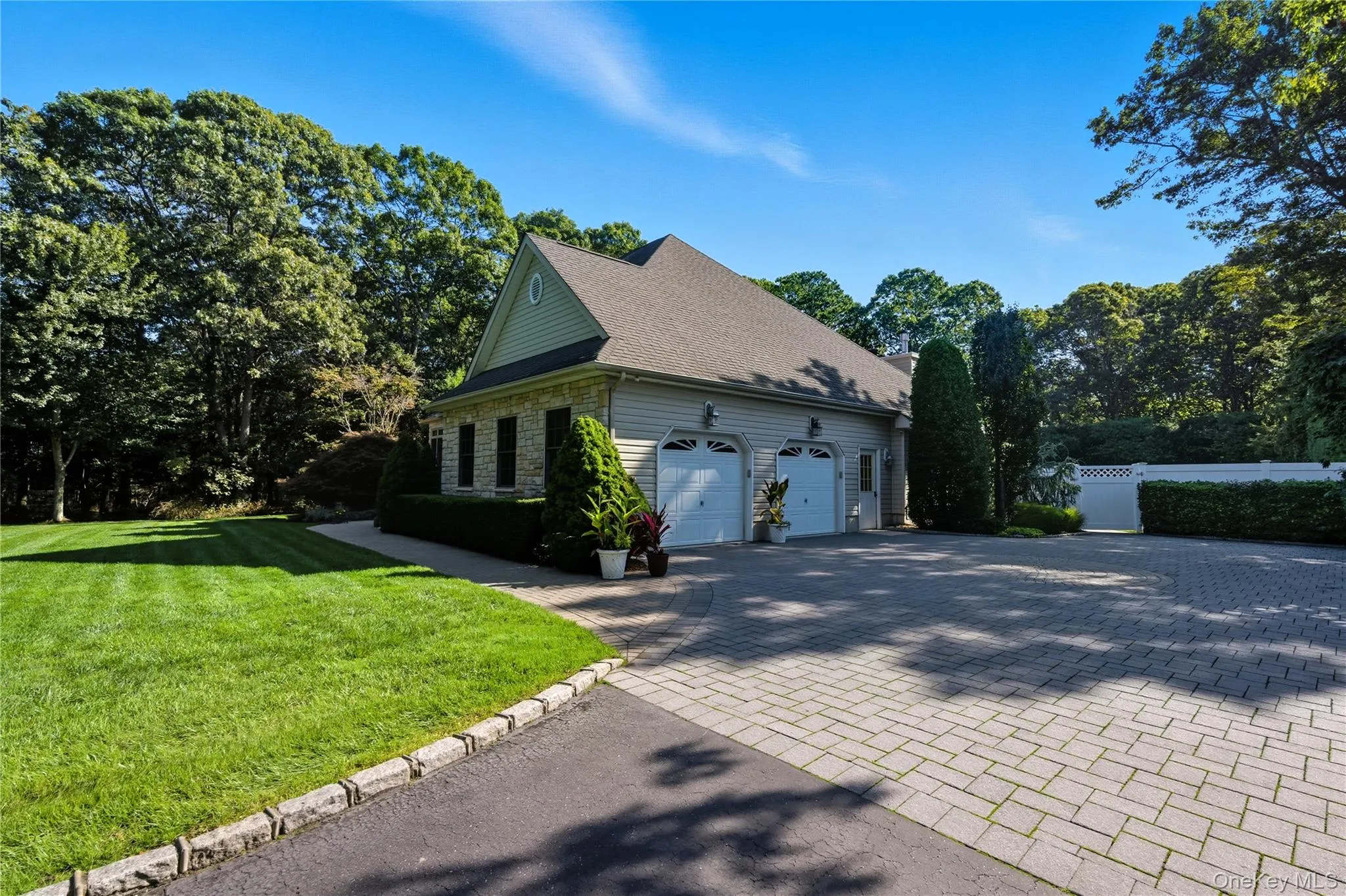View of home's exterior featuring stone siding, decorative driveway, a 2 garage, a yard, and view of wooded area View of home's exterior featuring stone siding, decorative driveway, a 2 garage, a yard, and view of wooded area
