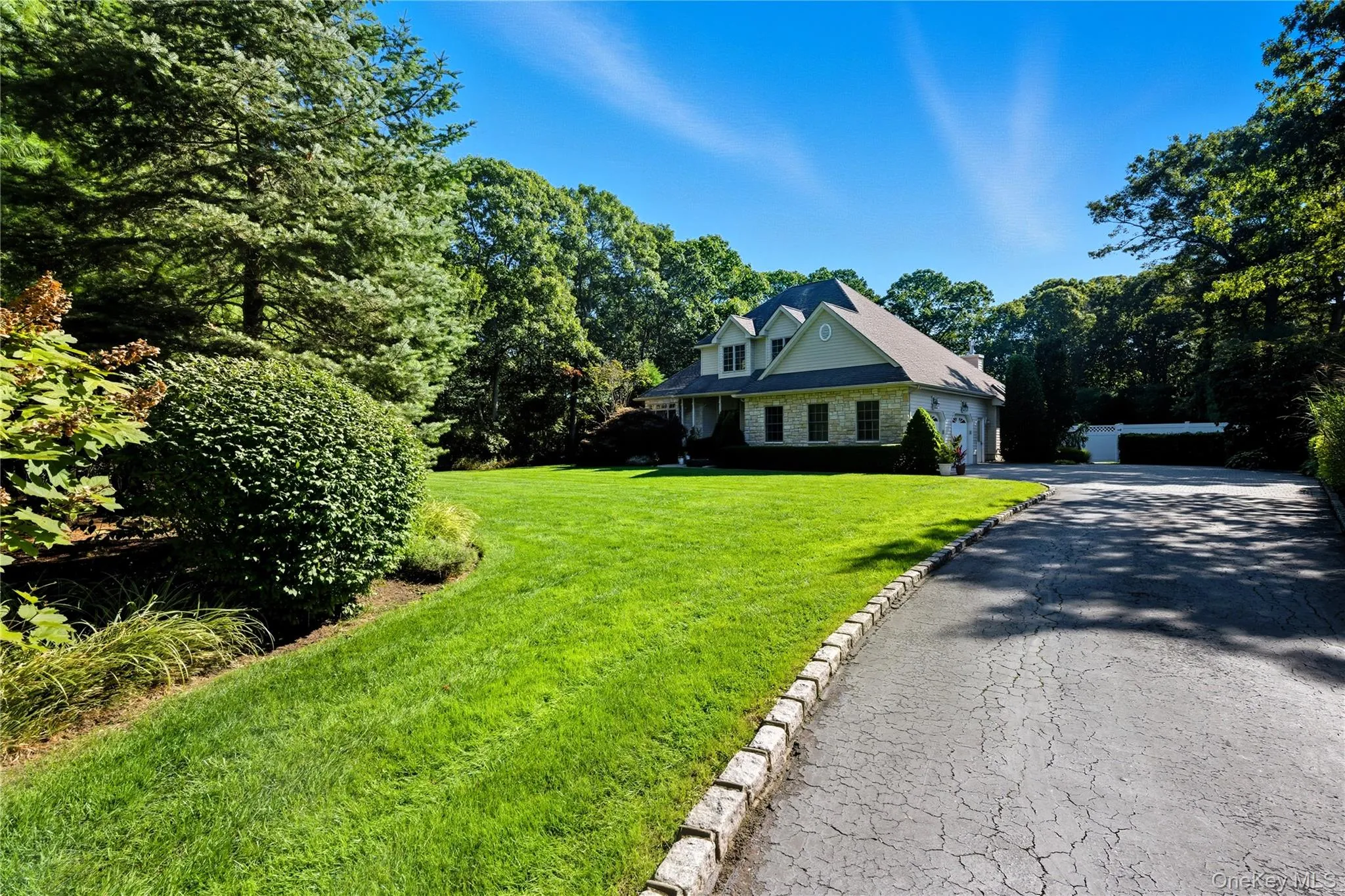 New england style home with a front yard, driveway, and view of wooded area New england style home with a front yard, driveway, and view of wooded area