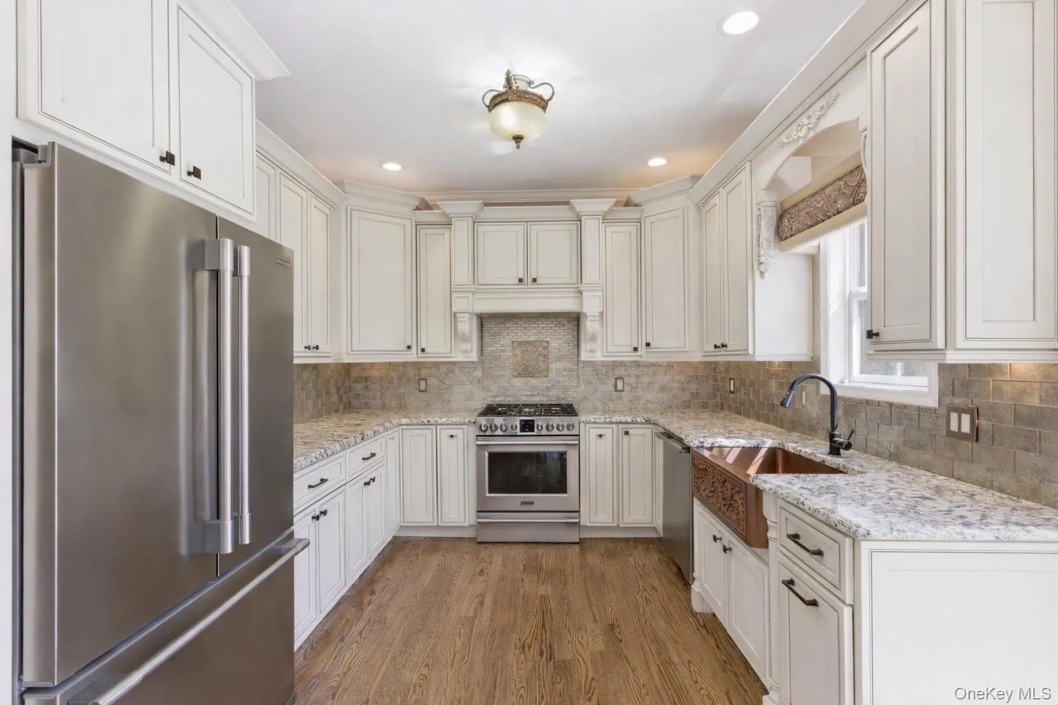 The kitchen features white cabinetry, granite countertops, stainless steel appliances, a tile backsplash, and a copper farmhouse sink The kitchen features white cabinetry, granite countertops, stainless steel appliances, a tile backsplash, and a copper farmhouse sink