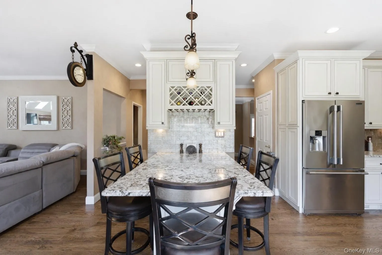 The kitchen features white cabinetry, a spacious island with a light-colored countertop, and a stainless steel refrigerator The kitchen features white cabinetry, a spacious island with a light-colored countertop, and a stainless steel refrigerator