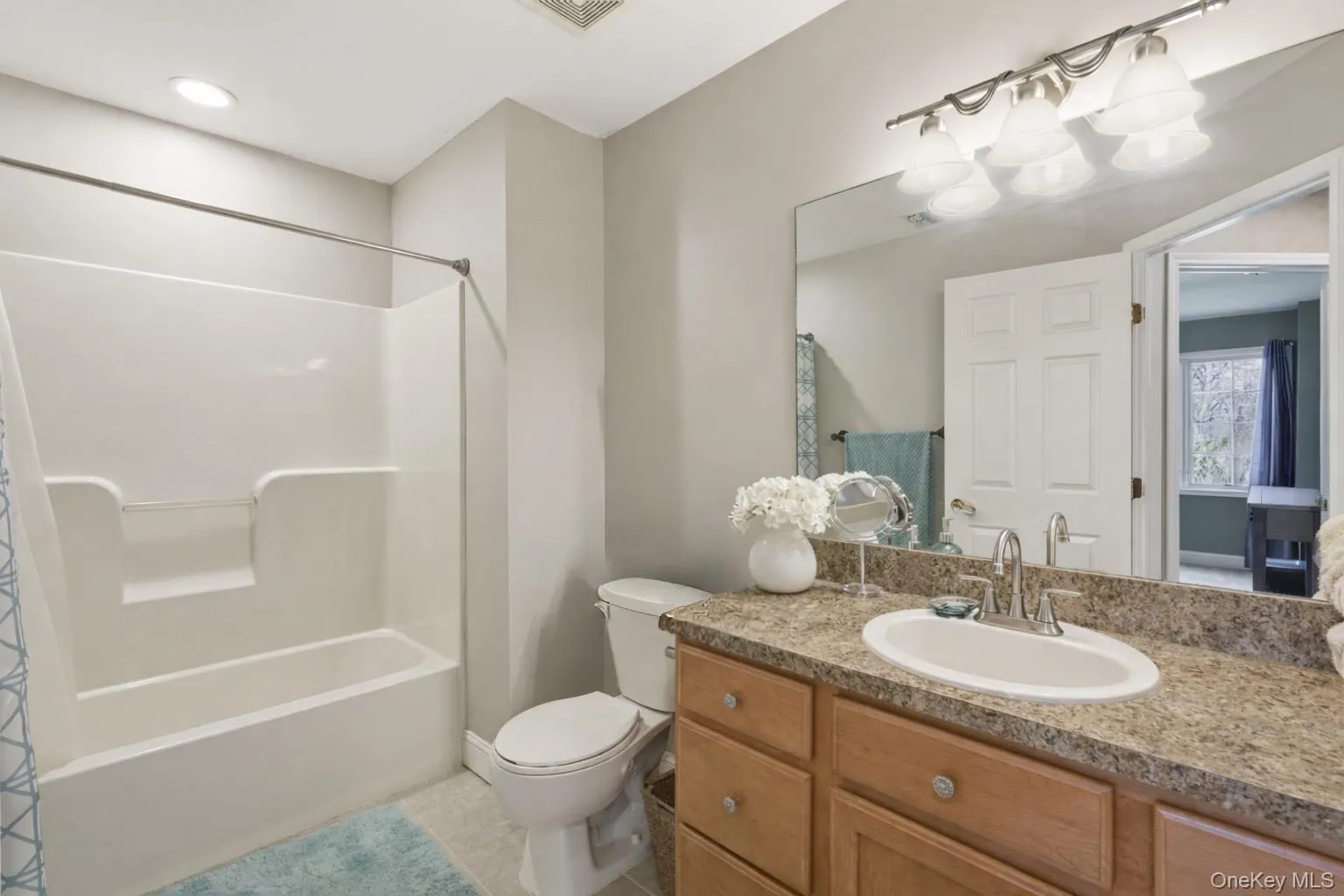 Bathroom featuring a white tub and shower combination, a vanity with a granite countertop, and a large mirror with overhead lighting Bathroom featuring a white tub and shower combination, a vanity with a granite countertop, and a large mirror with overhead lighting