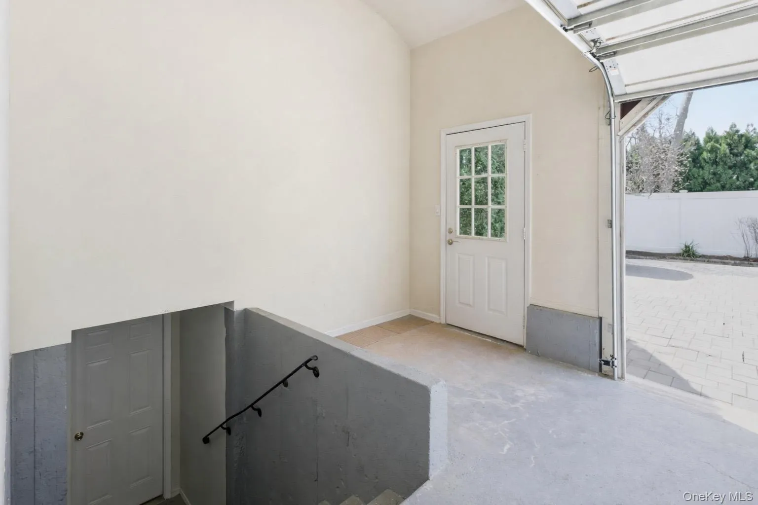 The property features an overhead garage door, a side entrance door with window panes, and interior stairs leading to the basement. The property features an overhead garage door, a side entrance door with window panes, and interior stairs leading to the basement.