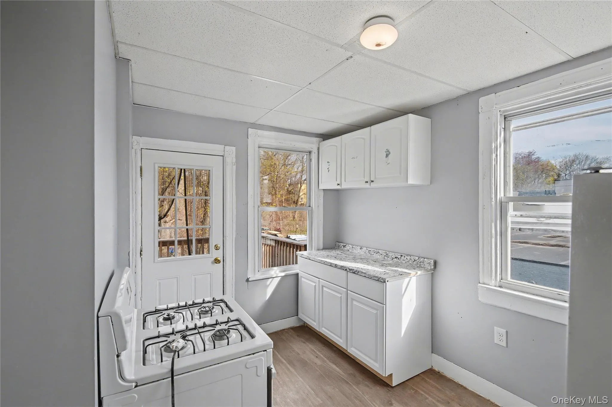 Kitchen featuring white cabinetry, white gas range, light countertops, light wood finished floors, and a drop ceiling Kitchen featuring white cabinetry, white gas range, light countertops, light wood finished floors, and a drop ceiling