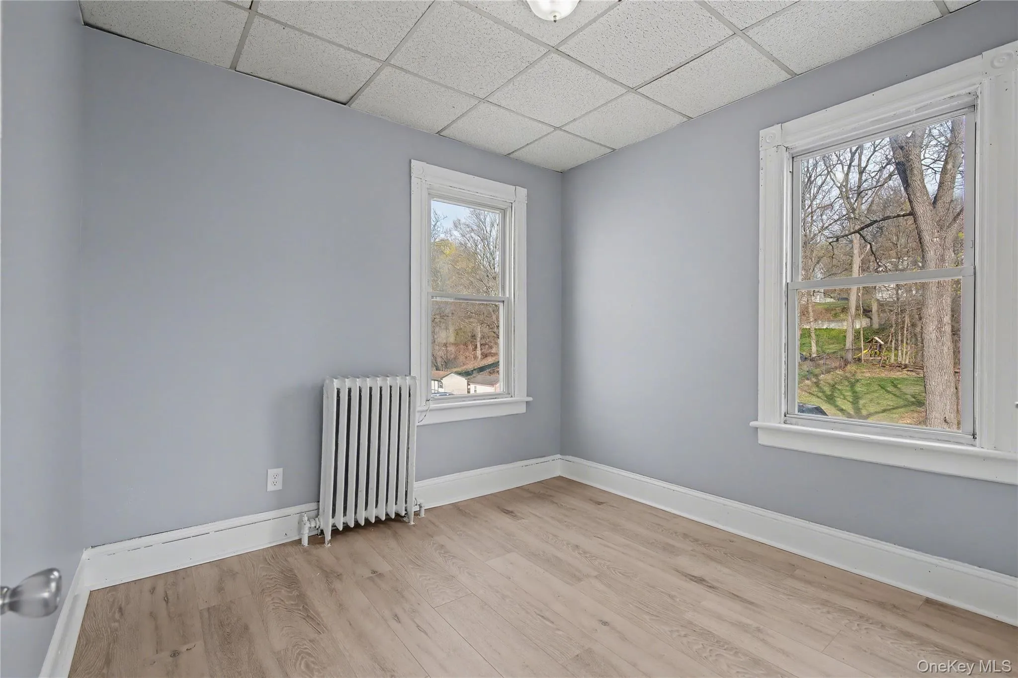 Empty room featuring radiator, a paneled ceiling, and light wood-style floors Empty room featuring radiator, a paneled ceiling, and light wood-style floors