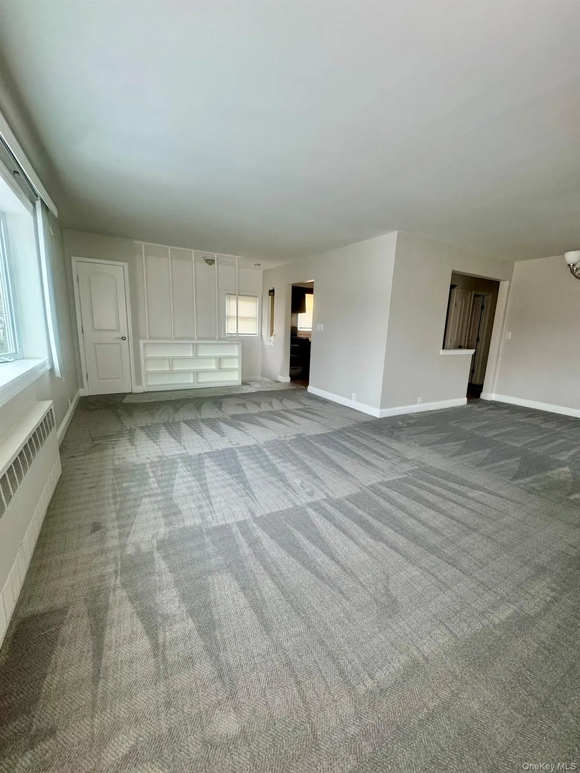 Unfurnished living room featuring radiator heating unit and grsy colored carpet Unfurnished living room featuring radiator heating unit and grsy colored carpet