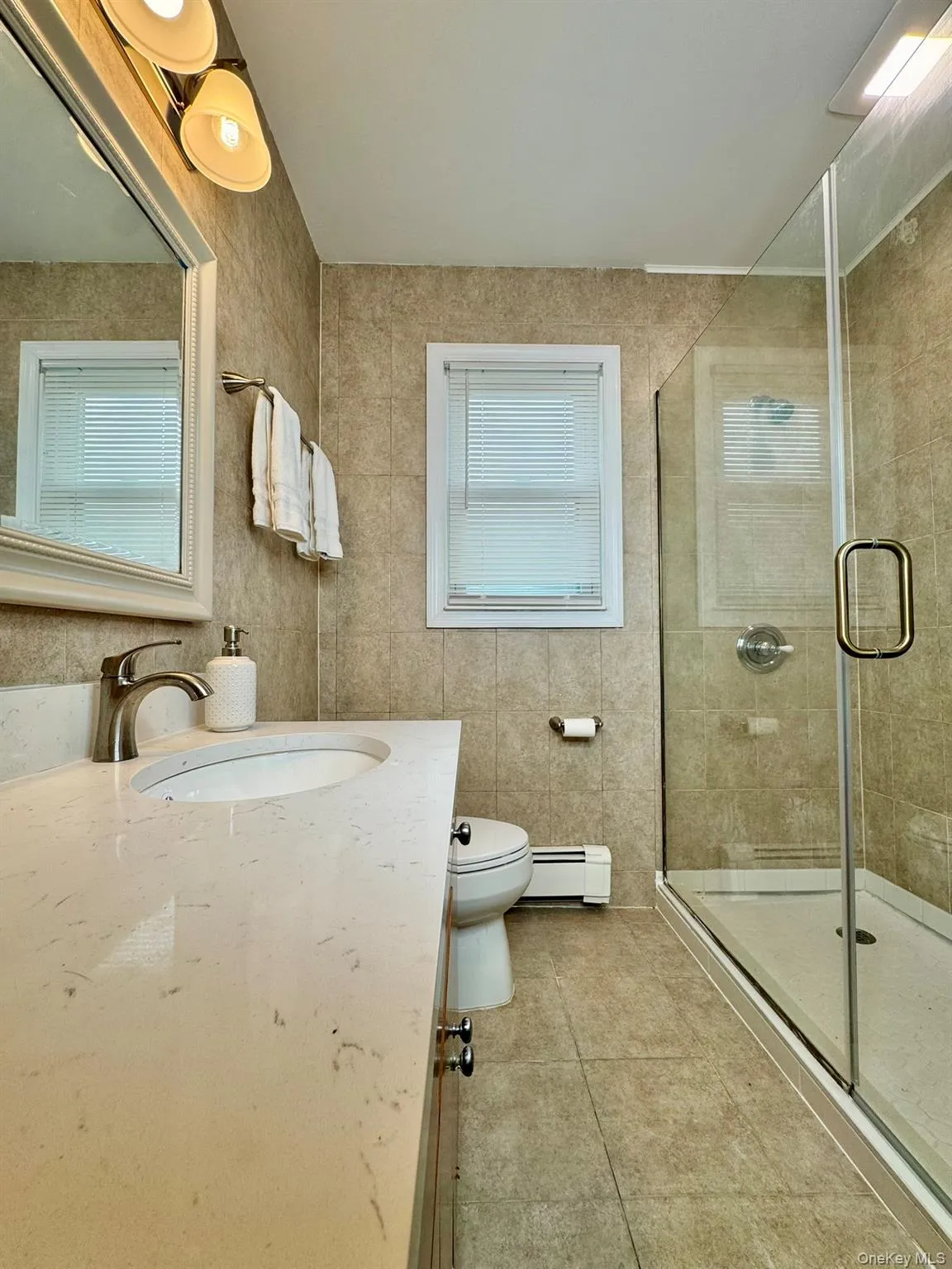 Full bath with vanity, a stall shower, light tile patterned floors, a baseboard radiator, and tile walls Full bath with vanity, a stall shower, light tile patterned floors, a baseboard radiator, and tile walls