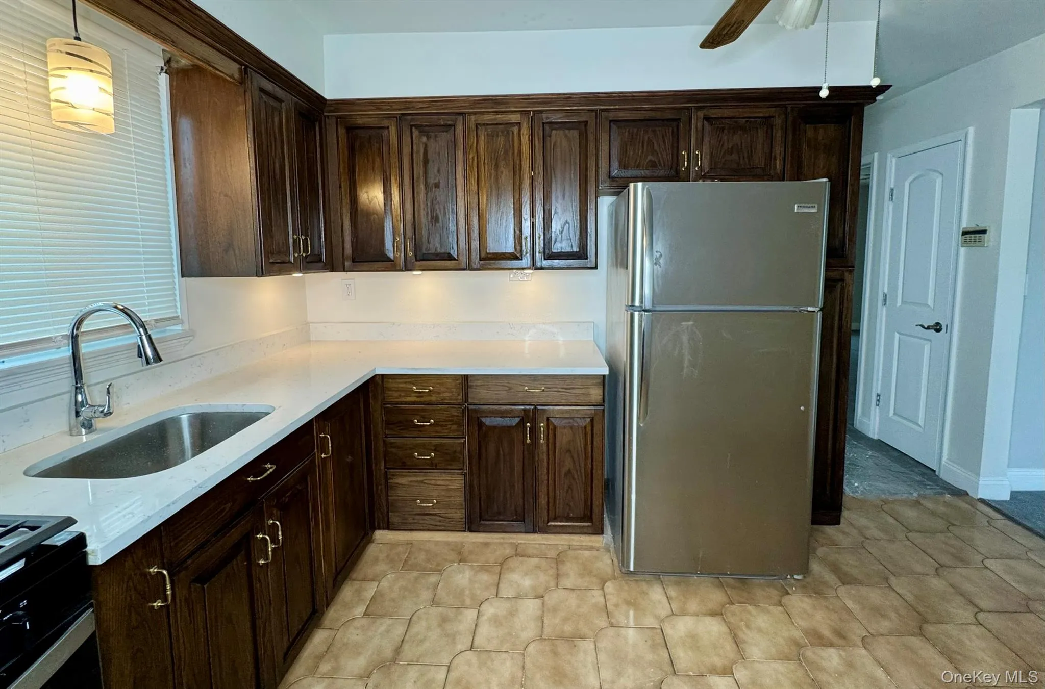 Kitchen with freestanding refrigerator, dark wood finish cabinetry, a ceiling fan, light stone counters, and range with gas stovetop Kitchen with freestanding refrigerator, dark wood finish cabinetry, a ceiling fan, light stone counters, and range with gas stovetop
