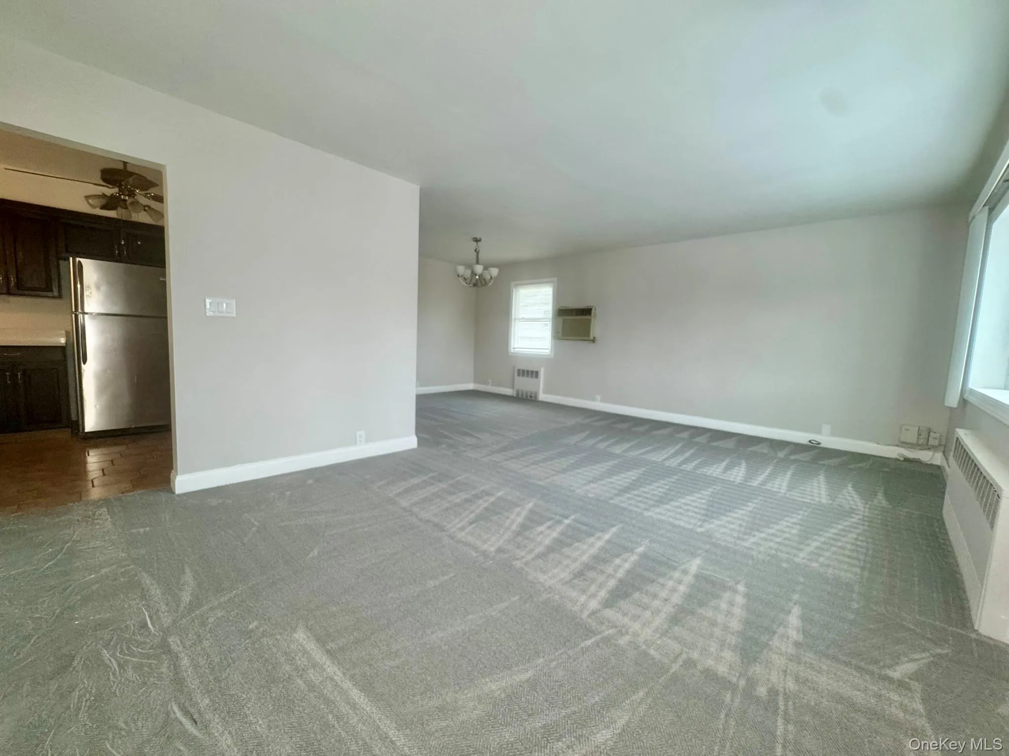 Unfurnished living room with a chandelier, gray carpet, radiator heating unit, and a ceiling fan Unfurnished living room with a chandelier, gray carpet, radiator heating unit, and a ceiling fan
