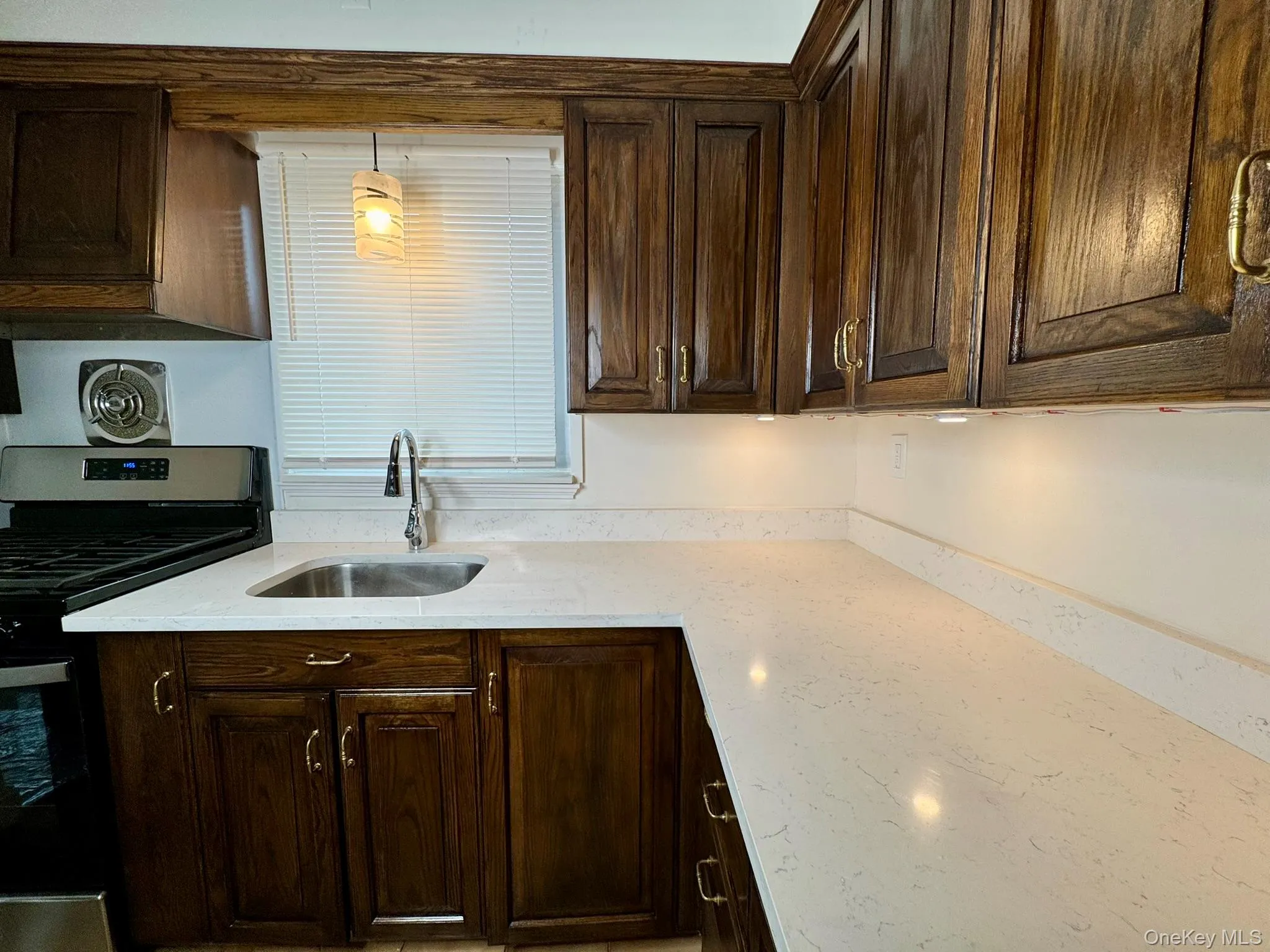 Kitchen featuring gas range, dark wood finish cabinetry, and light stone counters Kitchen featuring gas range, dark wood finish cabinetry, and light stone counters