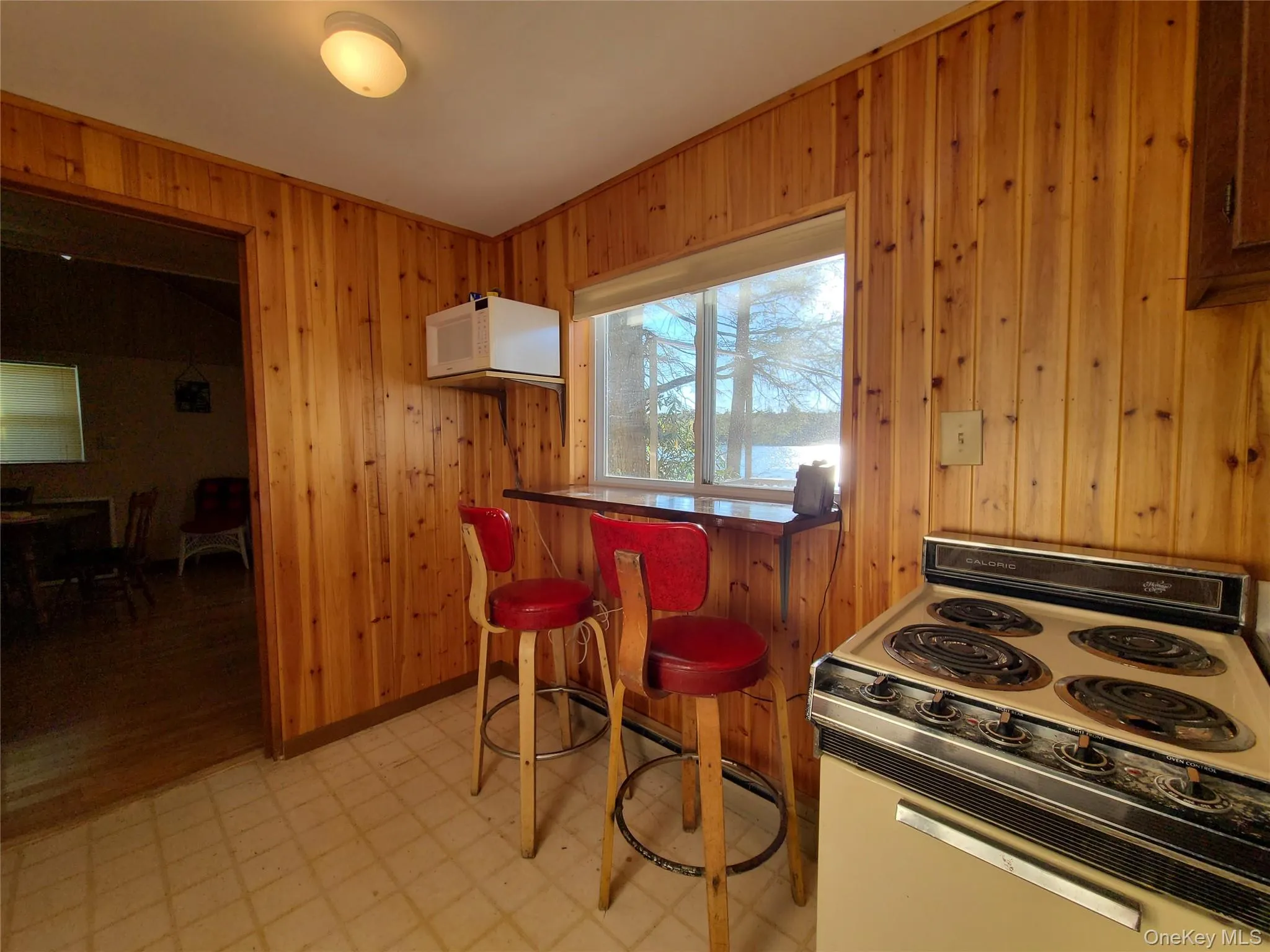 Kitchen featuring electric range, light flooring, wood walls, white microwave, and a breakfast bar Kitchen featuring electric range, light flooring, wood walls, white microwave, and a breakfast bar