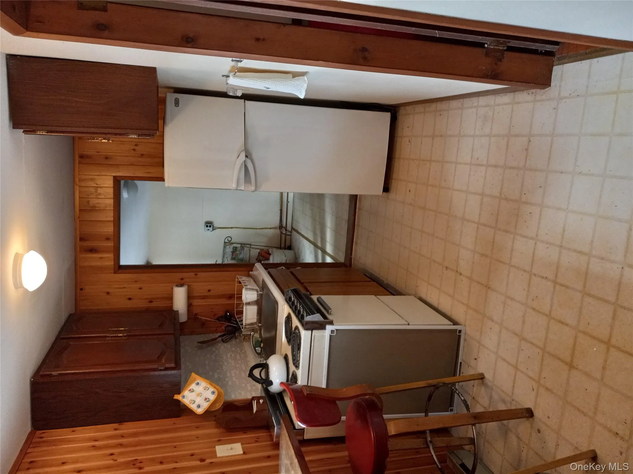 Kitchen featuring light floors, wooden walls, fridge, stove, and decorative backsplash Kitchen featuring light floors, wooden walls, fridge, stove, and decorative backsplash