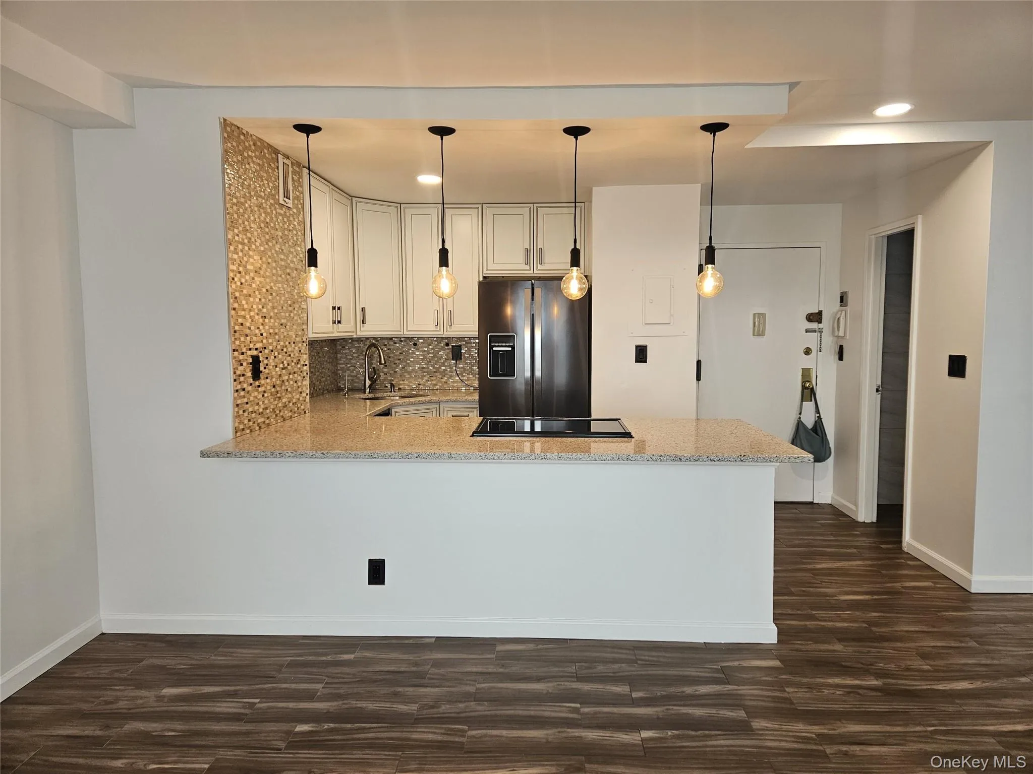 Kitchen with a peninsula, tasteful backsplash, a breakfast bar area, stainless steel refrigerator with ice dispenser, and dark tile-style flooring Kitchen with a peninsula, tasteful backsplash, a breakfast bar area, stainless steel refrigerator with ice dispenser, and dark tile-style flooring