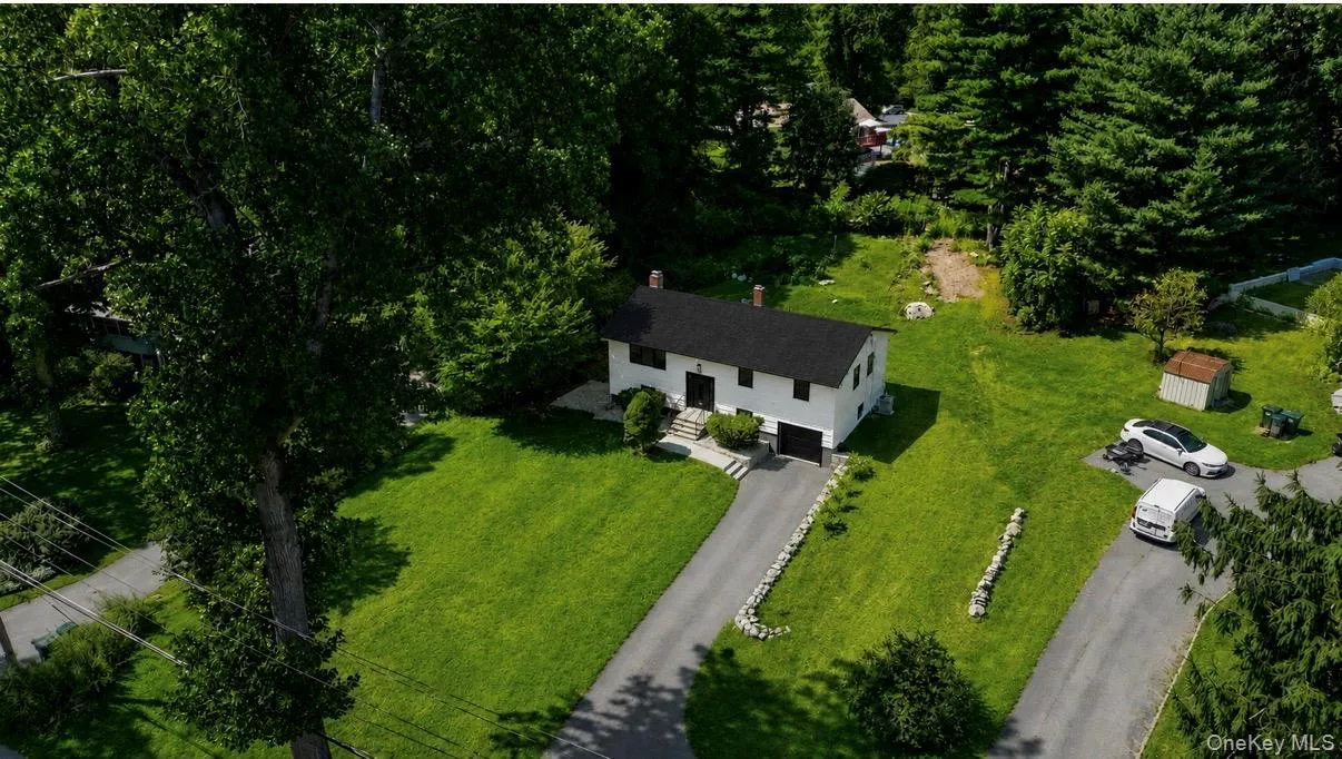Split-level residence featuring a dark shingle roof, white exterior, attached garage, and a paved driveway Split-level residence featuring a dark shingle roof, white exterior, attached garage, and a paved driveway