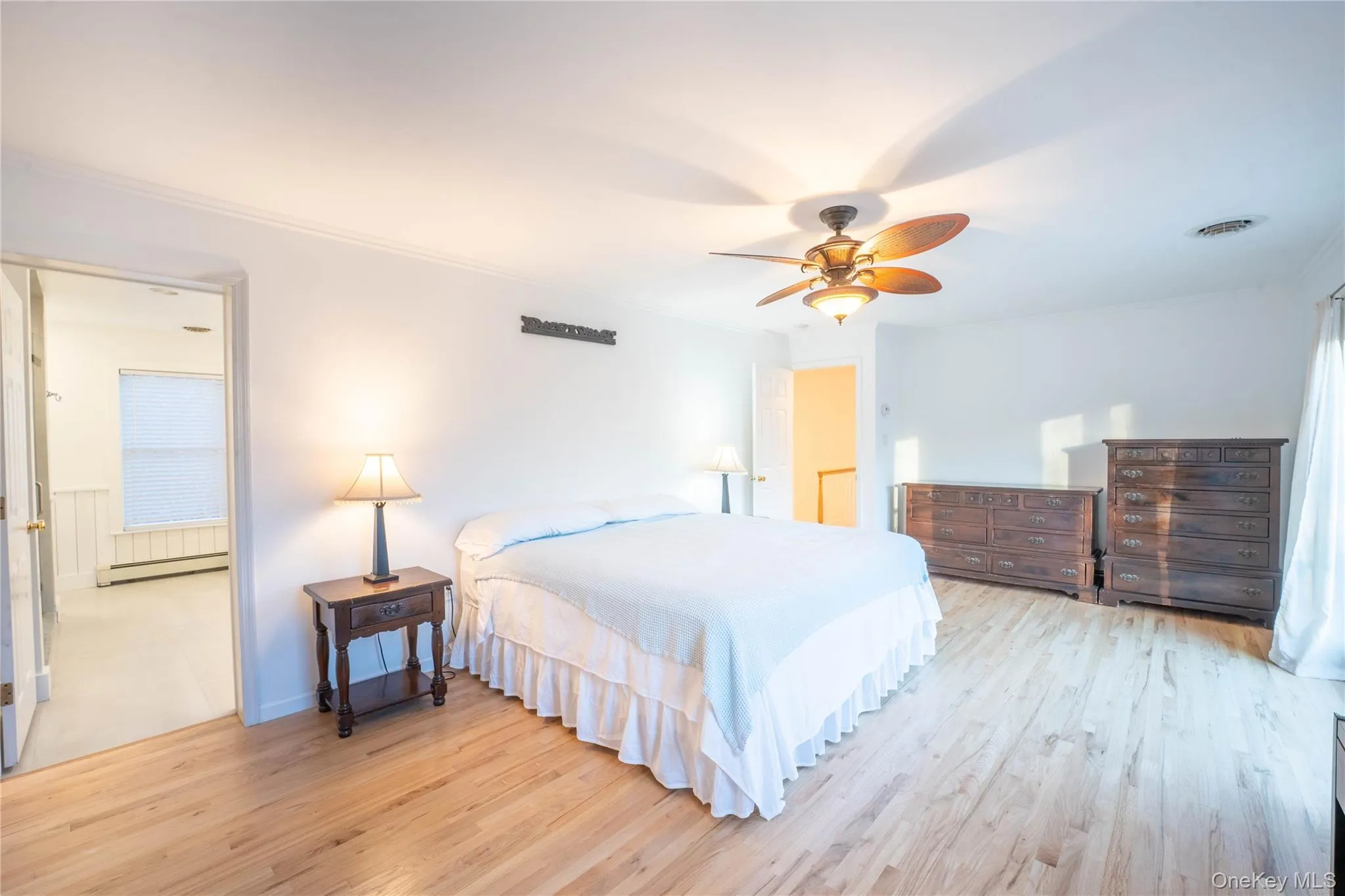 Bedroom featuring a baseboard radiator, light wood-style flooring, visible vents, a ceiling fan, and crown molding Bedroom featuring a baseboard radiator, light wood-style flooring, visible vents, a ceiling fan, and crown molding