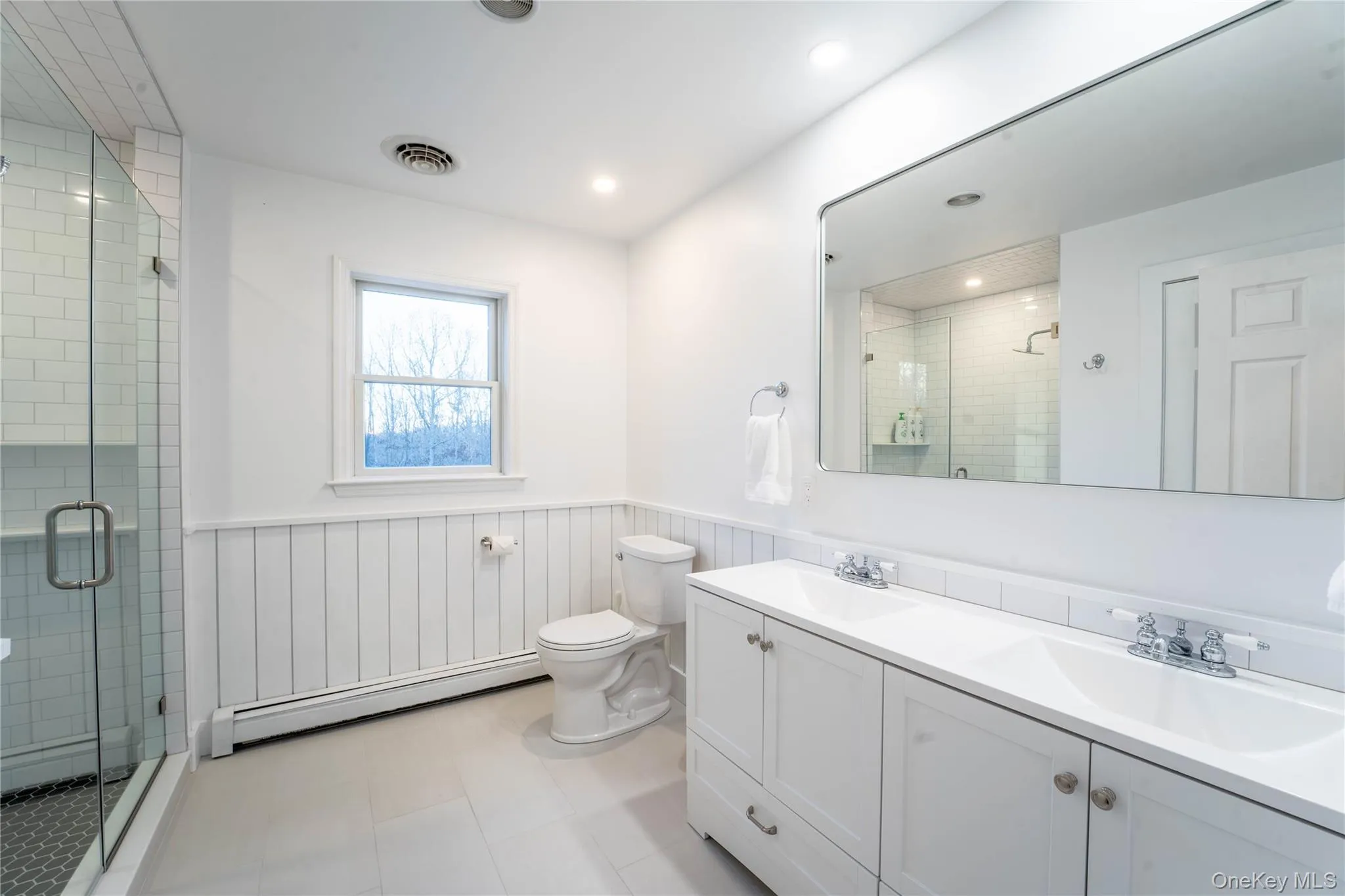 Full bath featuring a baseboard heating unit, a stall shower, a wainscoted wall, and a sink Full bath featuring a baseboard heating unit, a stall shower, a wainscoted wall, and a sink