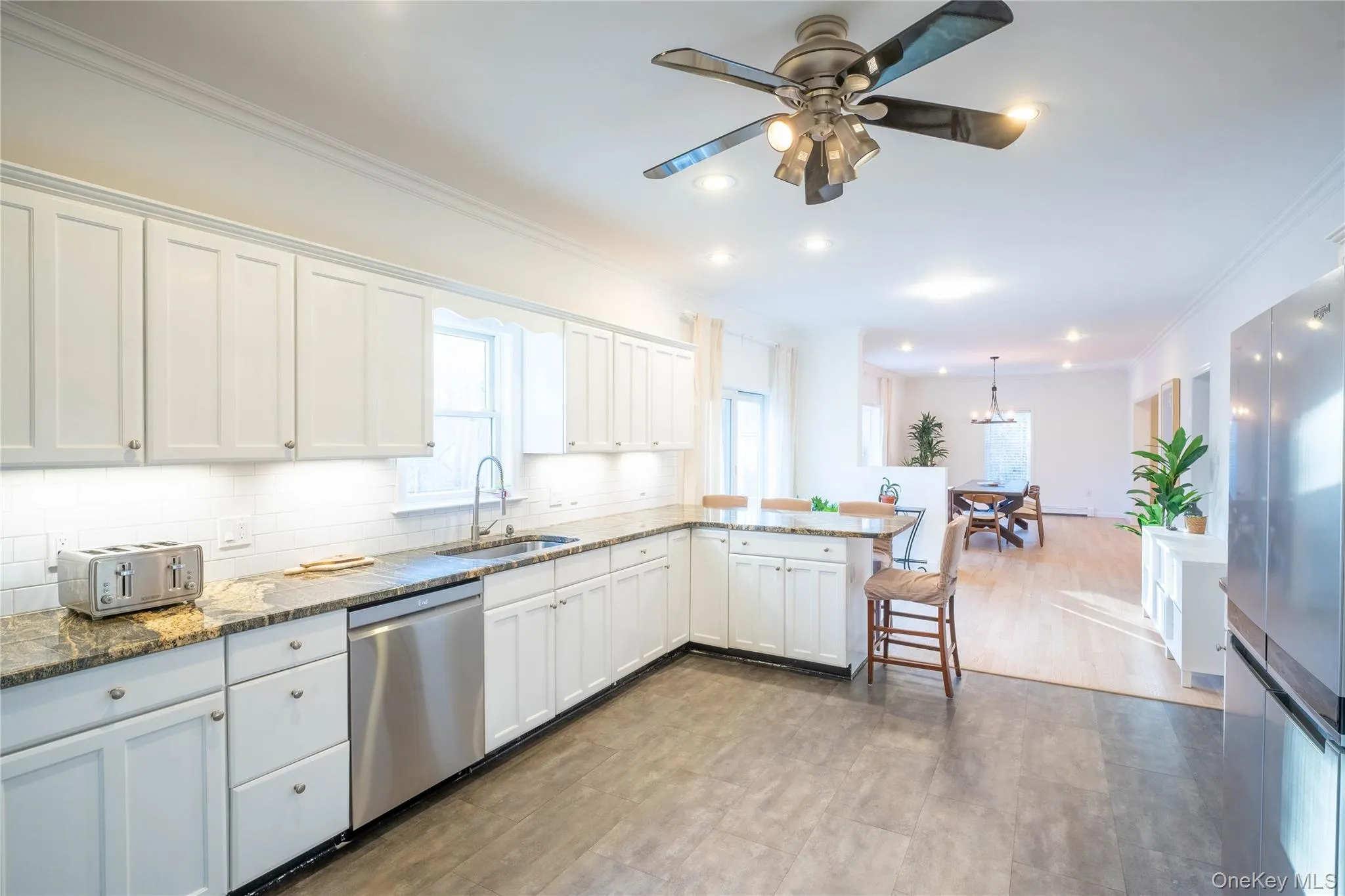 Kitchen with decorative backsplash, white cabinets, dishwasher, a peninsula, and a sink Kitchen with decorative backsplash, white cabinets, dishwasher, a peninsula, and a sink
