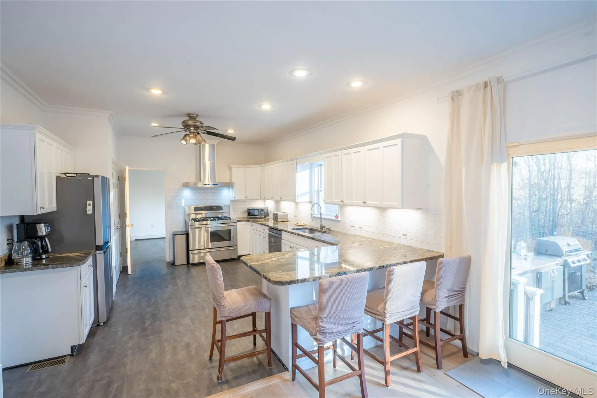 Kitchen with stainless steel appliances, white cabinetry, a sink, a peninsula, and wall chimney exhaust hood Kitchen with stainless steel appliances, white cabinetry, a sink, a peninsula, and wall chimney exhaust hood