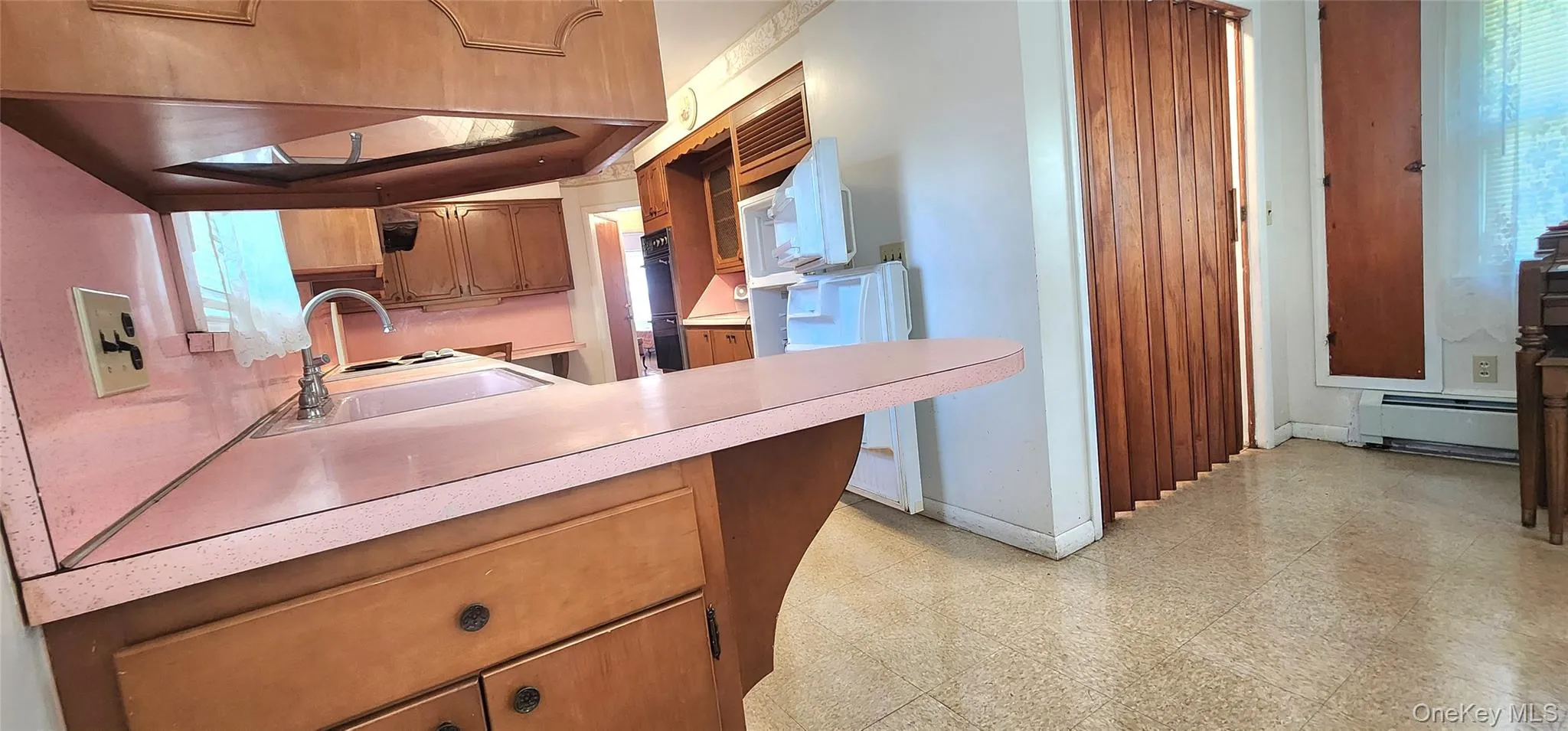 Kitchen featuring light floors, light countertops, a baseboard heating unit, brown cabinetry, and plenty of natural light Kitchen featuring light floors, light countertops, a baseboard heating unit, brown cabinetry, and plenty of natural light