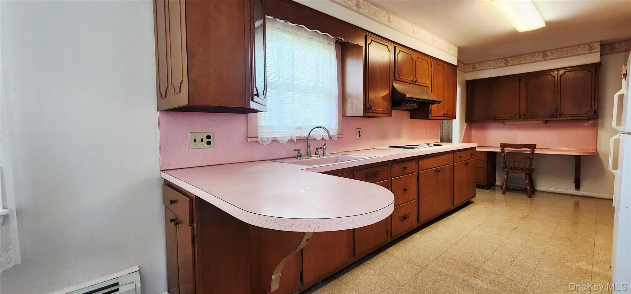Kitchen with light countertops, under cabinet range hood, a baseboard radiator, light floors, and a peninsula Kitchen with light countertops, under cabinet range hood, a baseboard radiator, light floors, and a peninsula