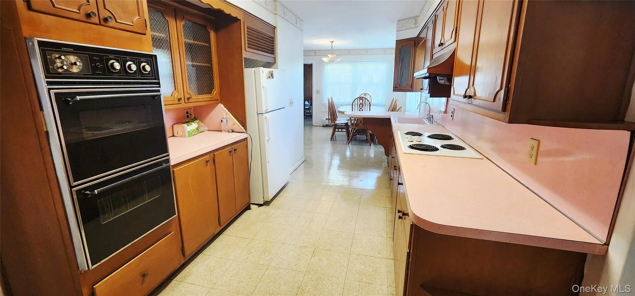 Kitchen featuring white appliances, light floors, light countertops, brown cabinets, and glass insert cabinets Kitchen featuring white appliances, light floors, light countertops, brown cabinets, and glass insert cabinets
