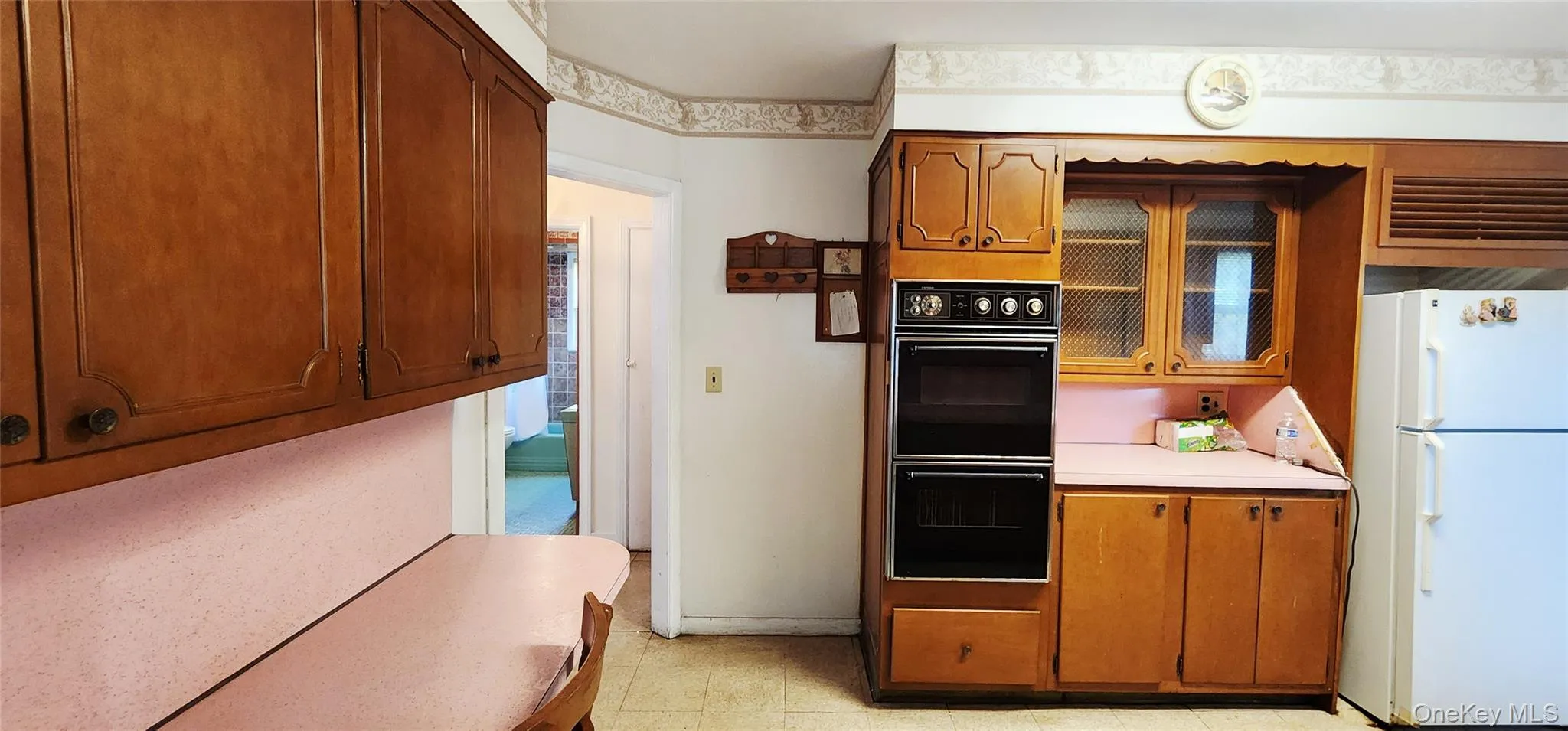 Kitchen with freestanding refrigerator, light countertops, brown cabinetry, and glass insert cabinets Kitchen with freestanding refrigerator, light countertops, brown cabinetry, and glass insert cabinets
