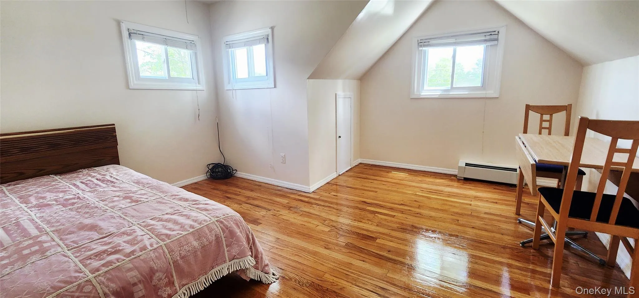 Bedroom featuring multiple windows, light wood-style floors, baseboard heating, and vaulted ceiling Bedroom featuring multiple windows, light wood-style floors, baseboard heating, and vaulted ceiling