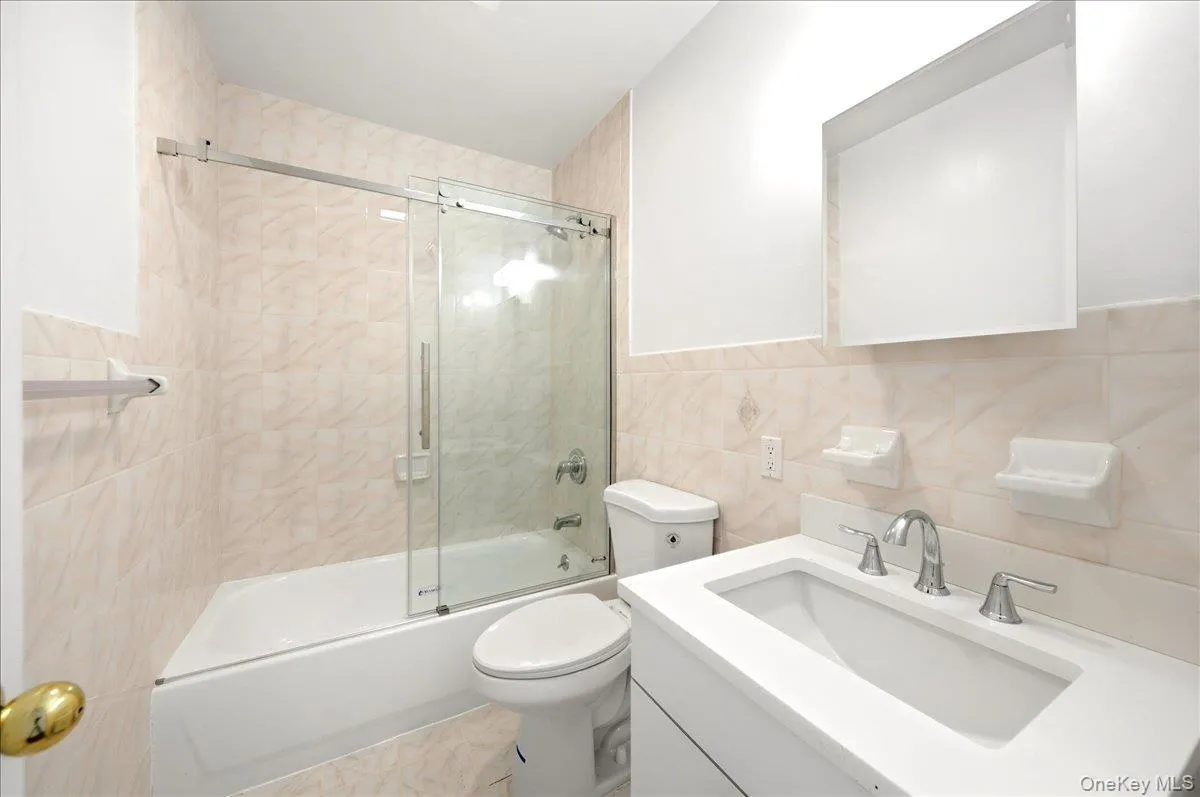 Bathroom with tile walls, vanity, and shower / bath combination with glass door Bathroom with tile walls, vanity, and shower / bath combination with glass door