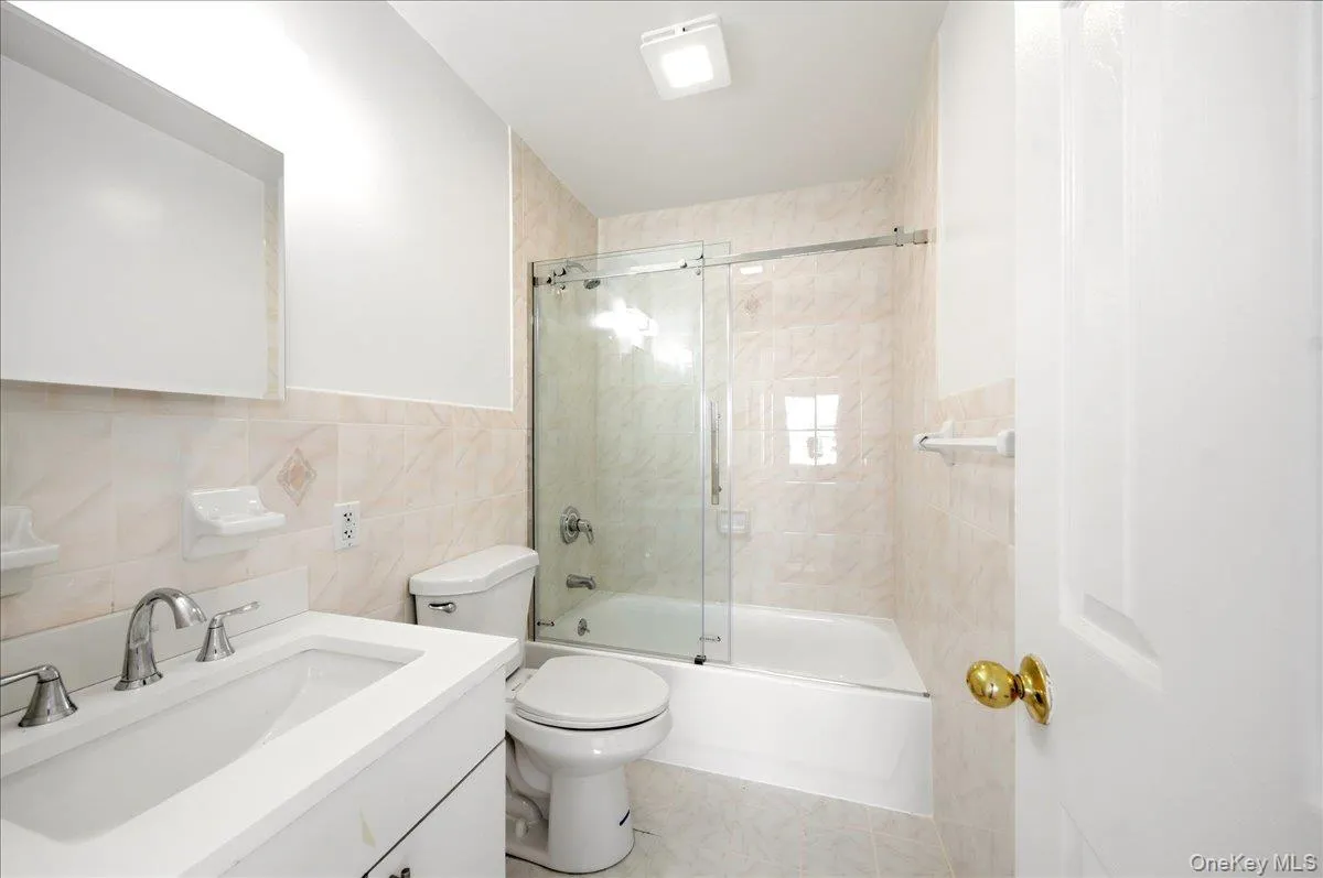 Full bath with tile walls, vanity, and shower / bath combination with glass door Full bath with tile walls, vanity, and shower / bath combination with glass door