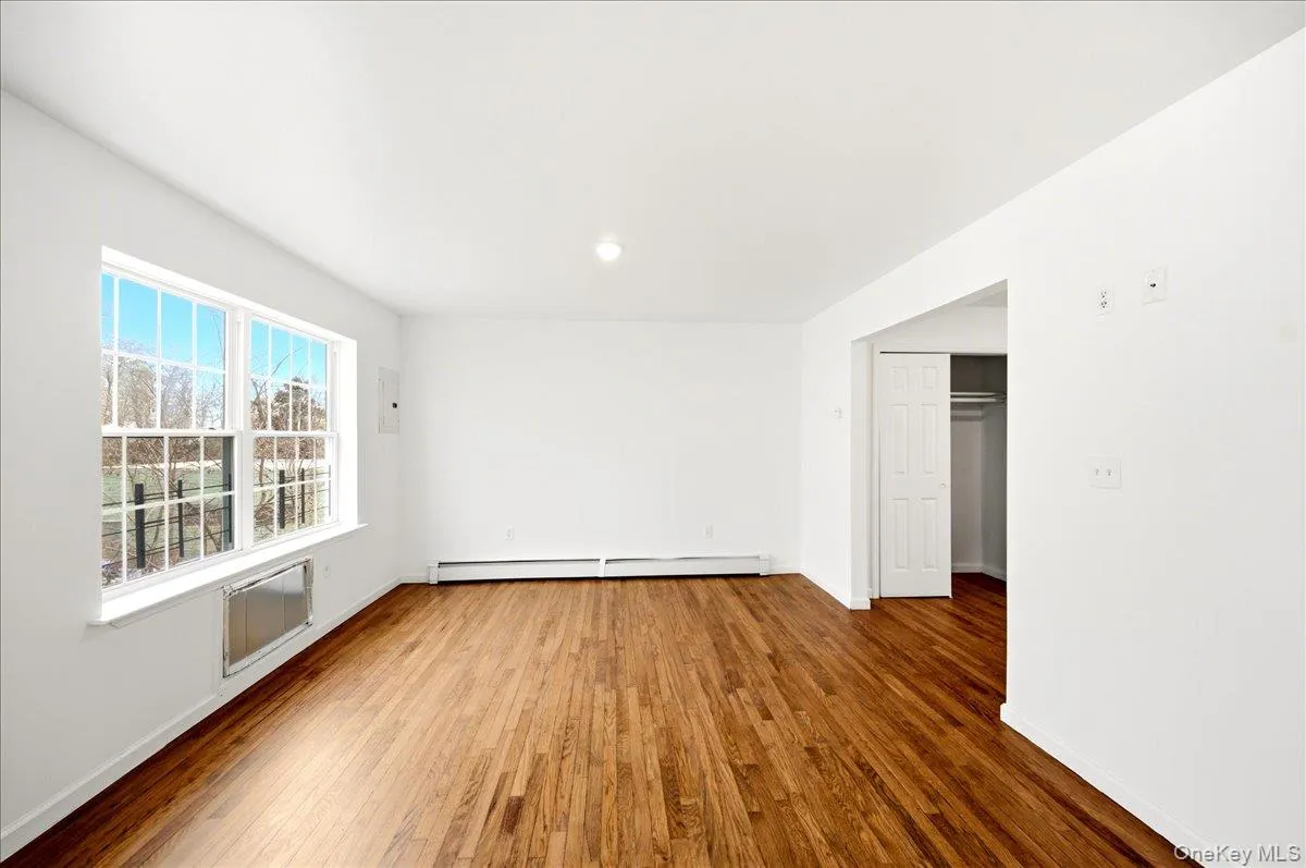 Empty room with dark wood-type flooring and a baseboard radiator Empty room with dark wood-type flooring and a baseboard radiator