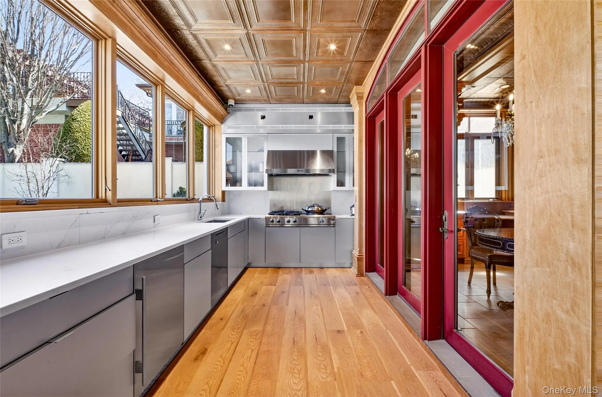 Kitchen featuring gray cabinetry, light wood-type flooring, light countertops, an ornate ceiling, and decorative backsplash Kitchen featuring gray cabinetry, light wood-type flooring, light countertops, an ornate ceiling, and decorative backsplash