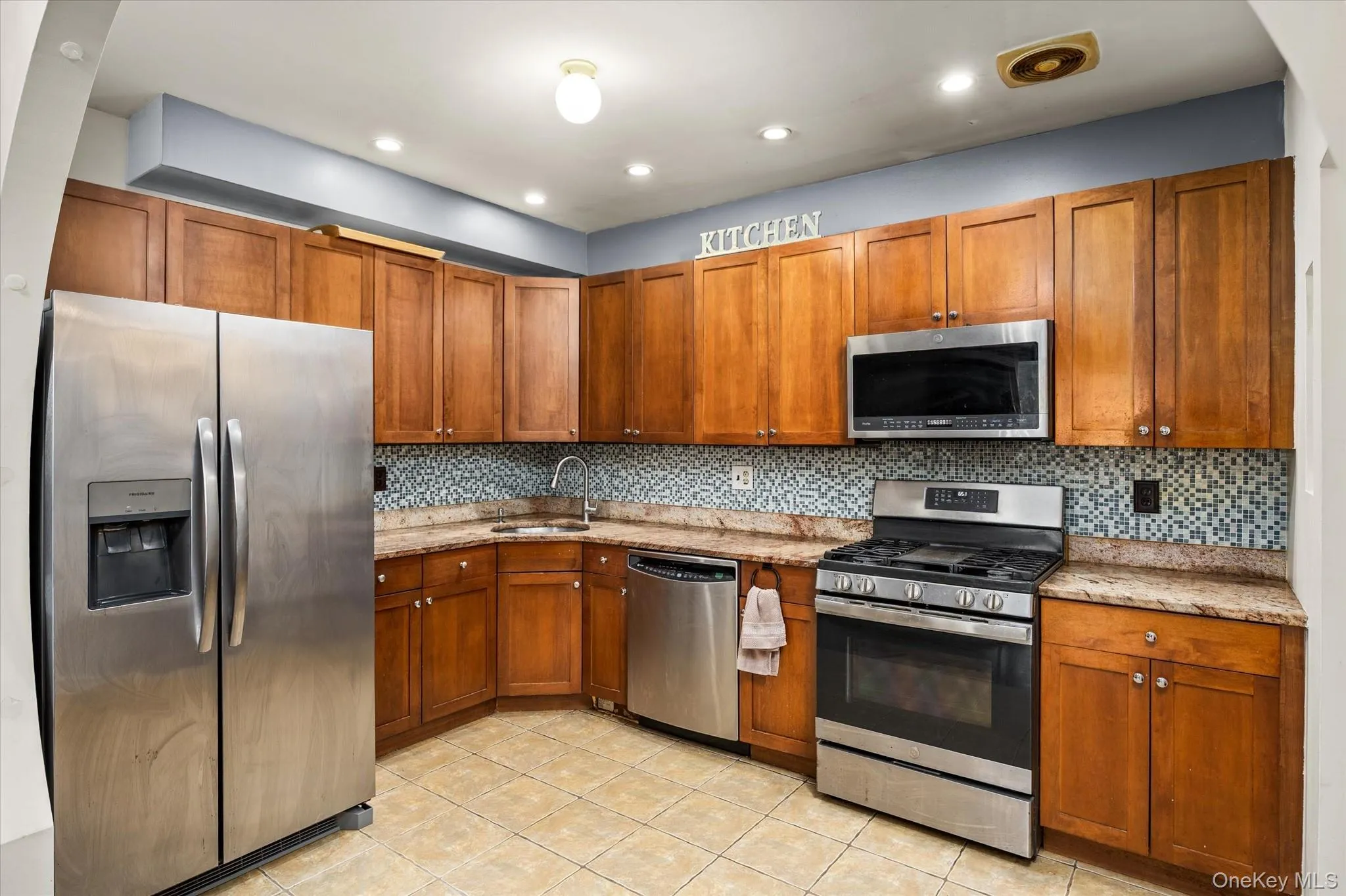 Kitchen featuring wood cabinetry, stainless steel appliances, mosaic tile backsplash, and light-toned countertops Kitchen featuring wood cabinetry, stainless steel appliances, mosaic tile backsplash, and light-toned countertops