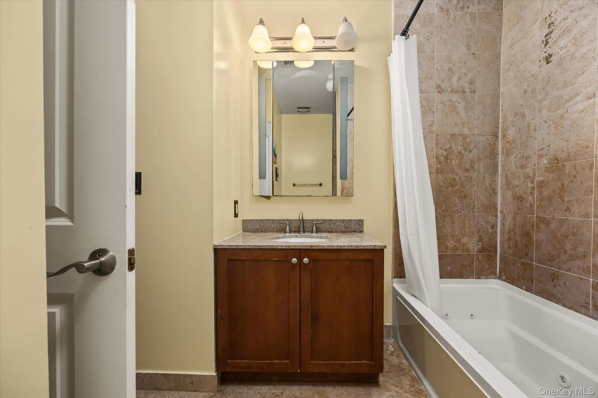 Bathroom featuring a wood vanity with a light-toned countertop, an integrated sink, and a wall-mounted mirror with overhead lighting Bathroom featuring a wood vanity with a light-toned countertop, an integrated sink, and a wall-mounted mirror with overhead lighting