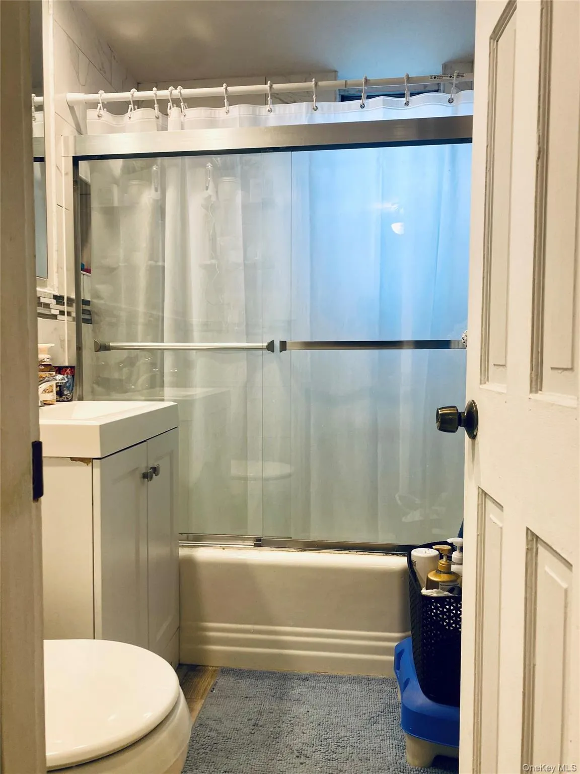 Bathroom featuring a white vanity with integrated sink, toilet, and a bathtub with sliding glass doors Bathroom featuring a white vanity with integrated sink, toilet, and a bathtub with sliding glass doors
