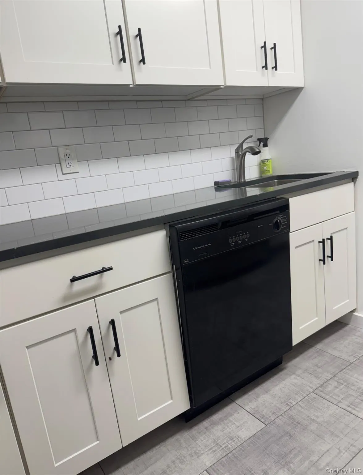 Kitchen with black dishwasher, white cabinets, and tasteful backsplash Kitchen with black dishwasher, white cabinets, and tasteful backsplash